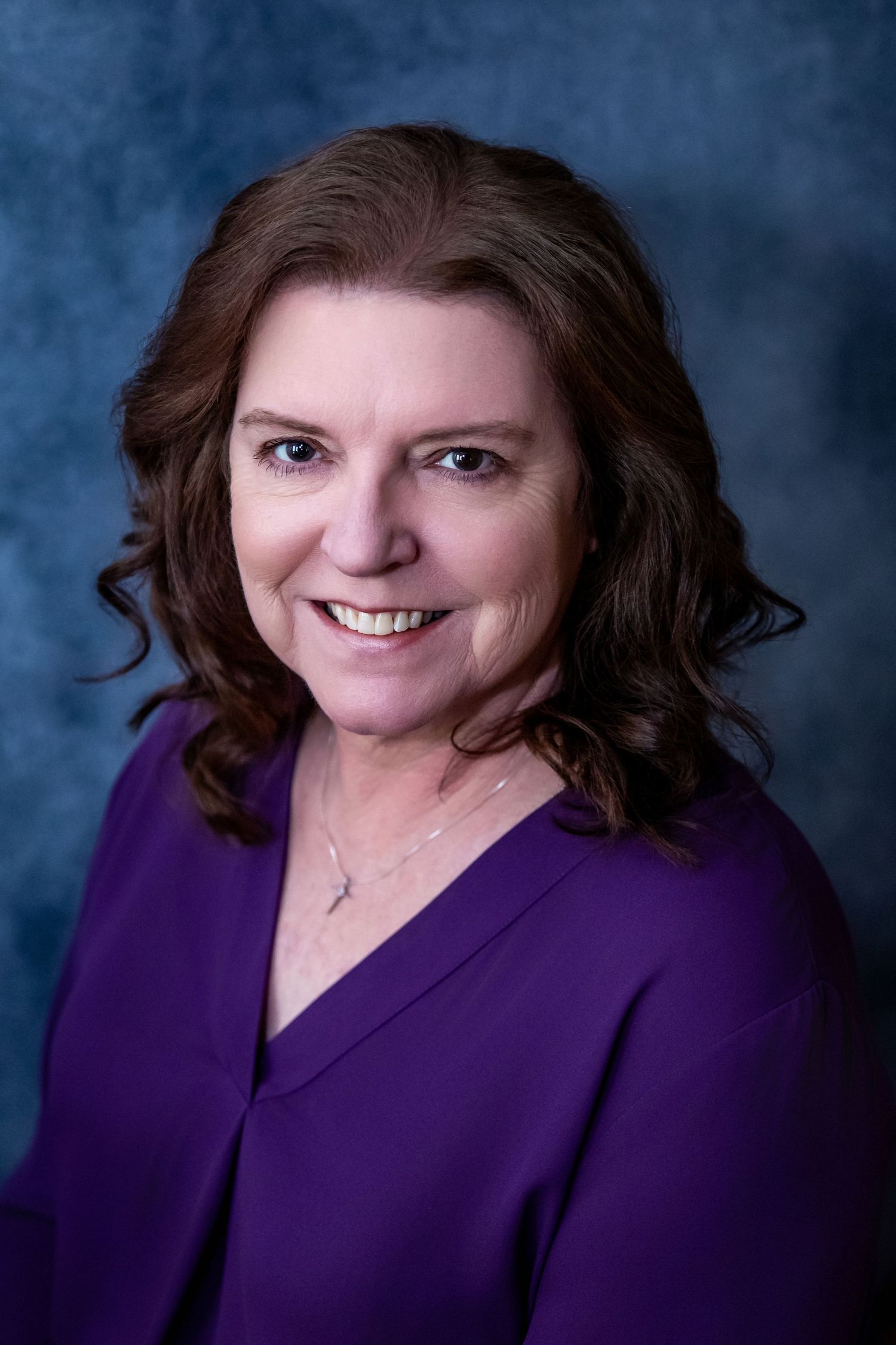 Professional portrait against blue backdrop wearing purple business attire.
