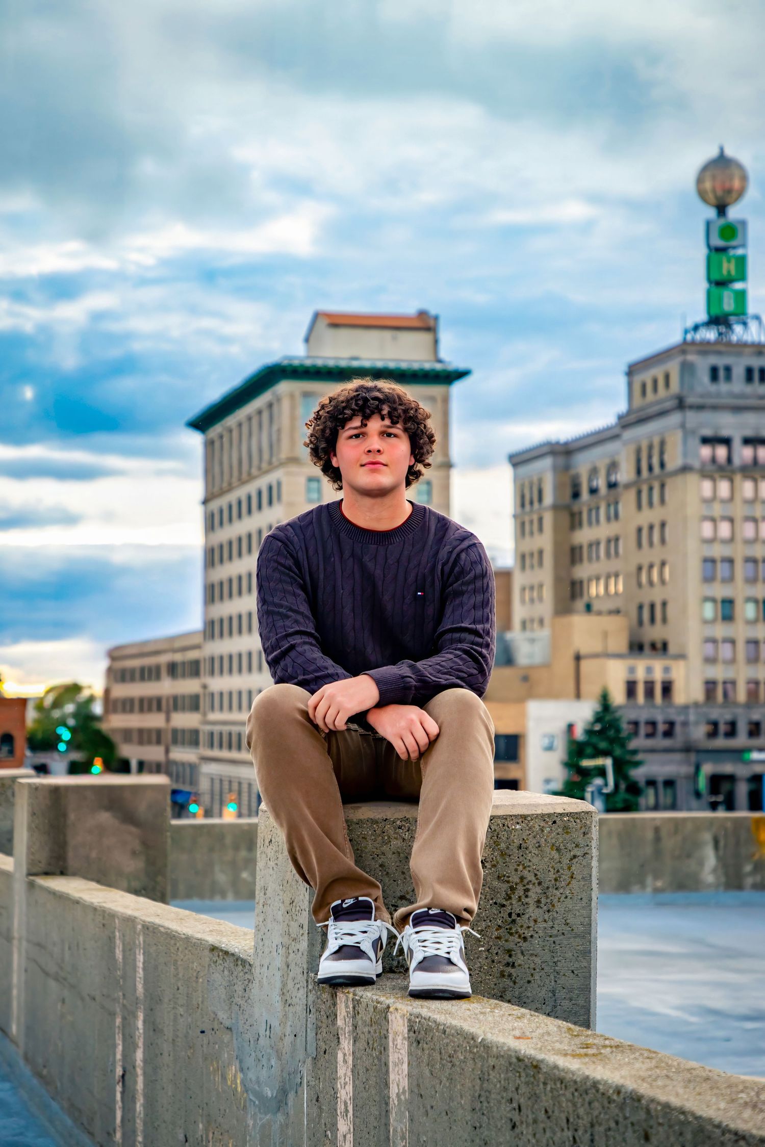 Person seated on concrete wall with urban cityscape and cloudy sky in background.