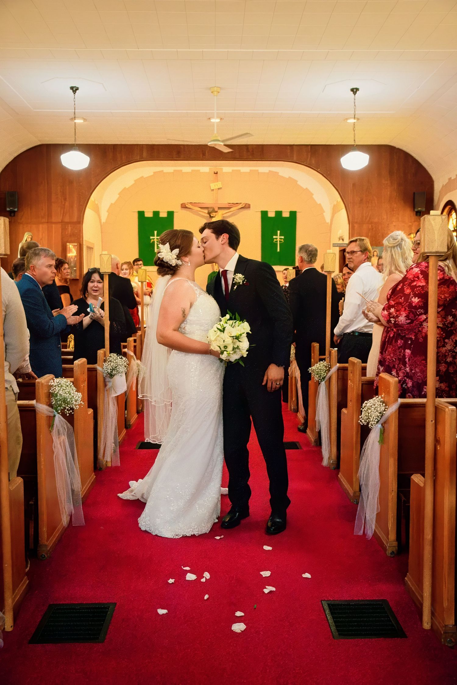 Wedding ceremony procession down red-carpeted church aisle with white rose petals scattered on the floor.