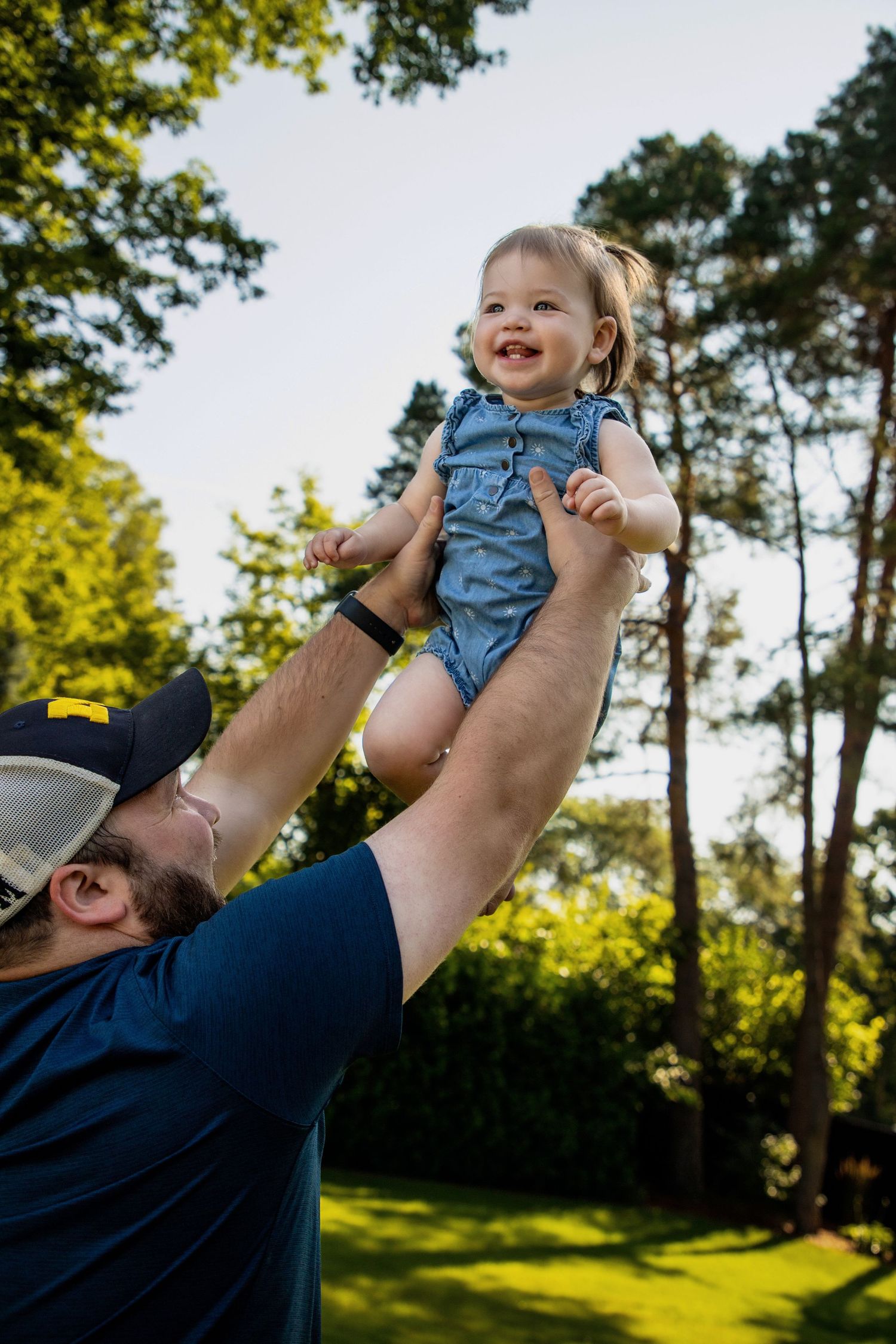 Joyful outdoor playtime scene with lifted child against sunny summer backdrop.