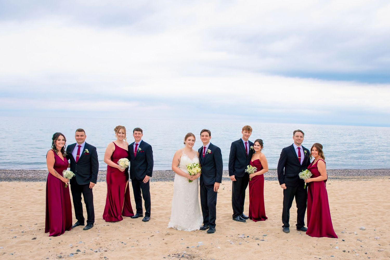 Wedding party members arranged in creative sitting poses along a scenic beach shoreline.