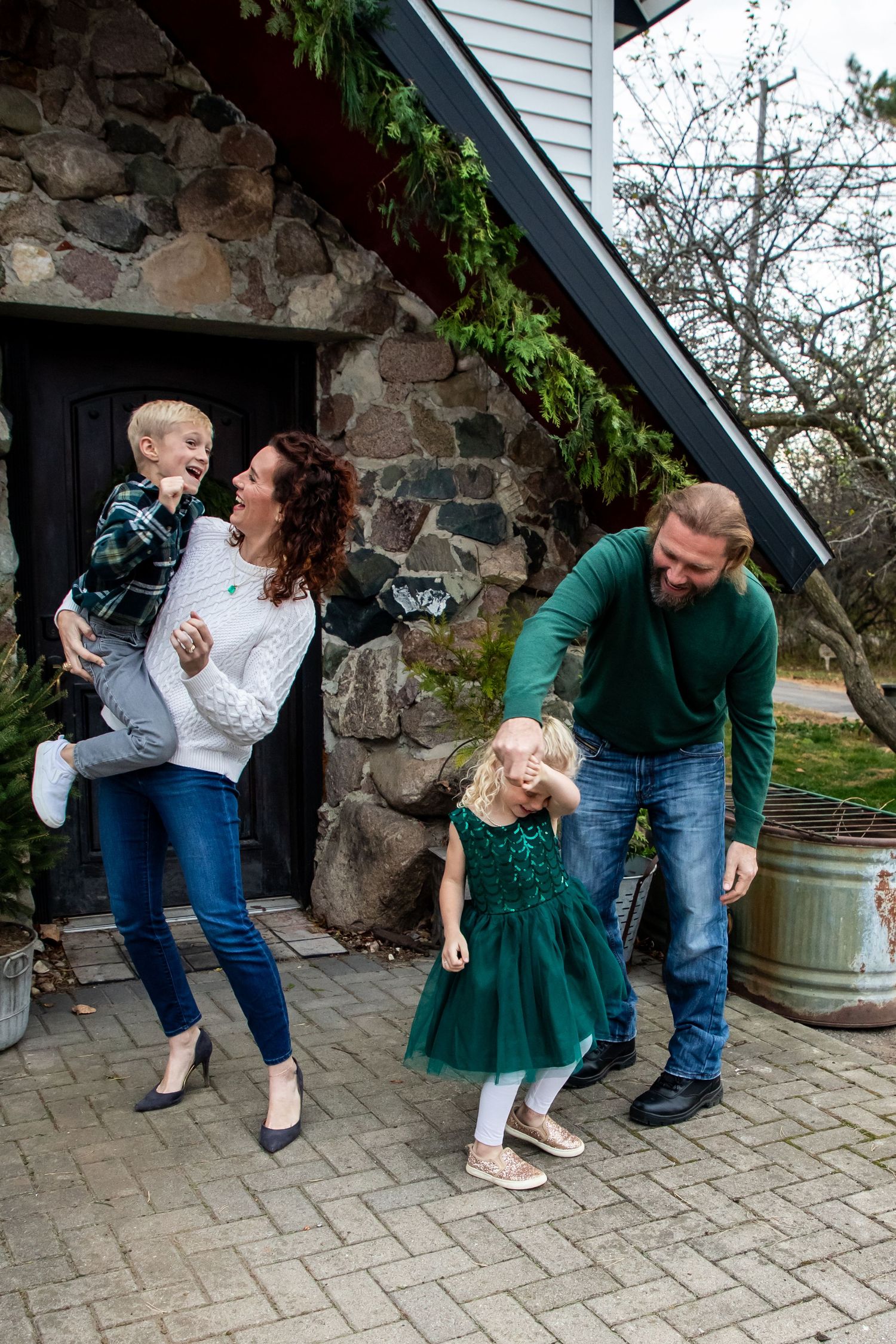 Candid family moment outside stone house with parents and children playing together.