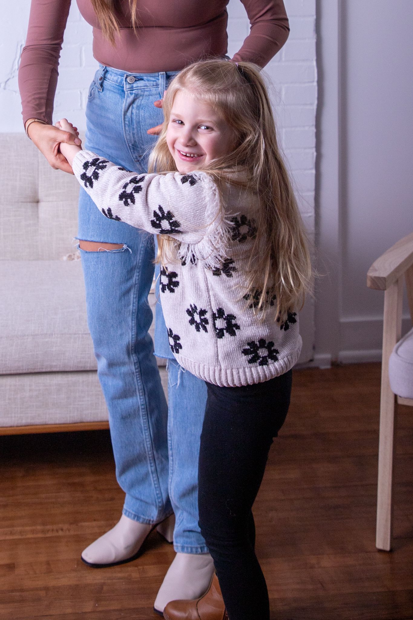 Child wearing floral sweater playing and dancing on hardwood floor.
