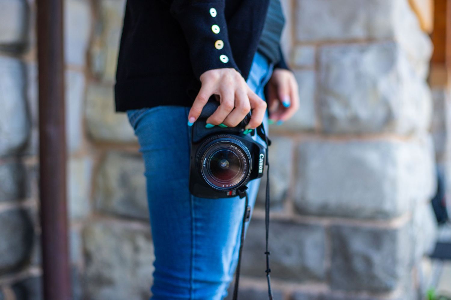 Close-up shot of hands holding professional camera against stone wall background.