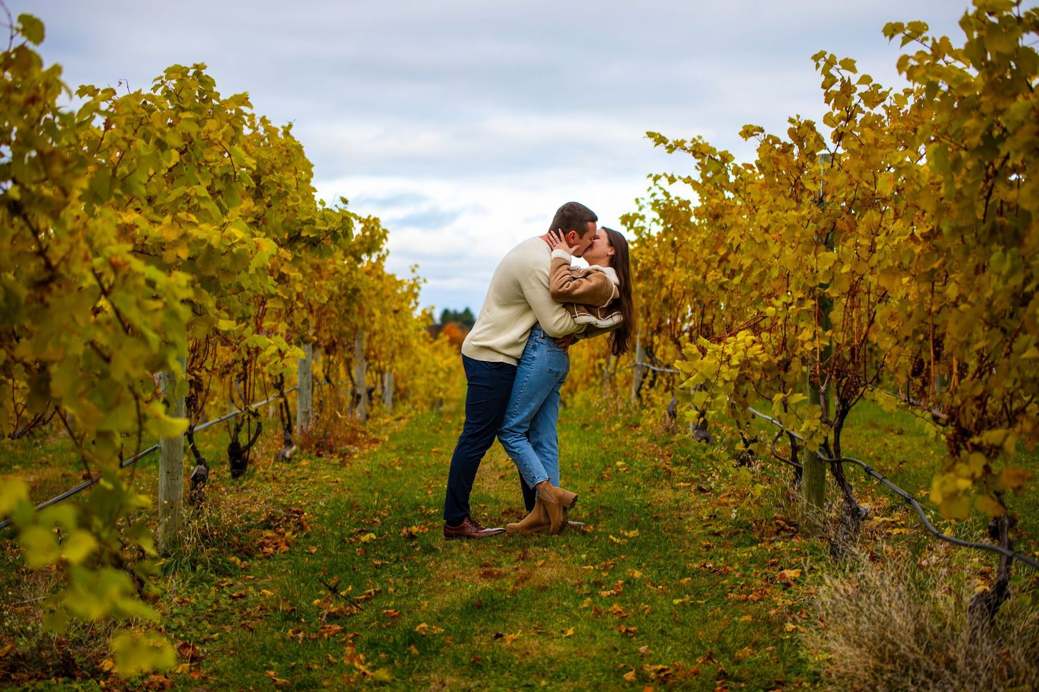 Playful couple walking through golden vineyard rows during autumn harvest season.