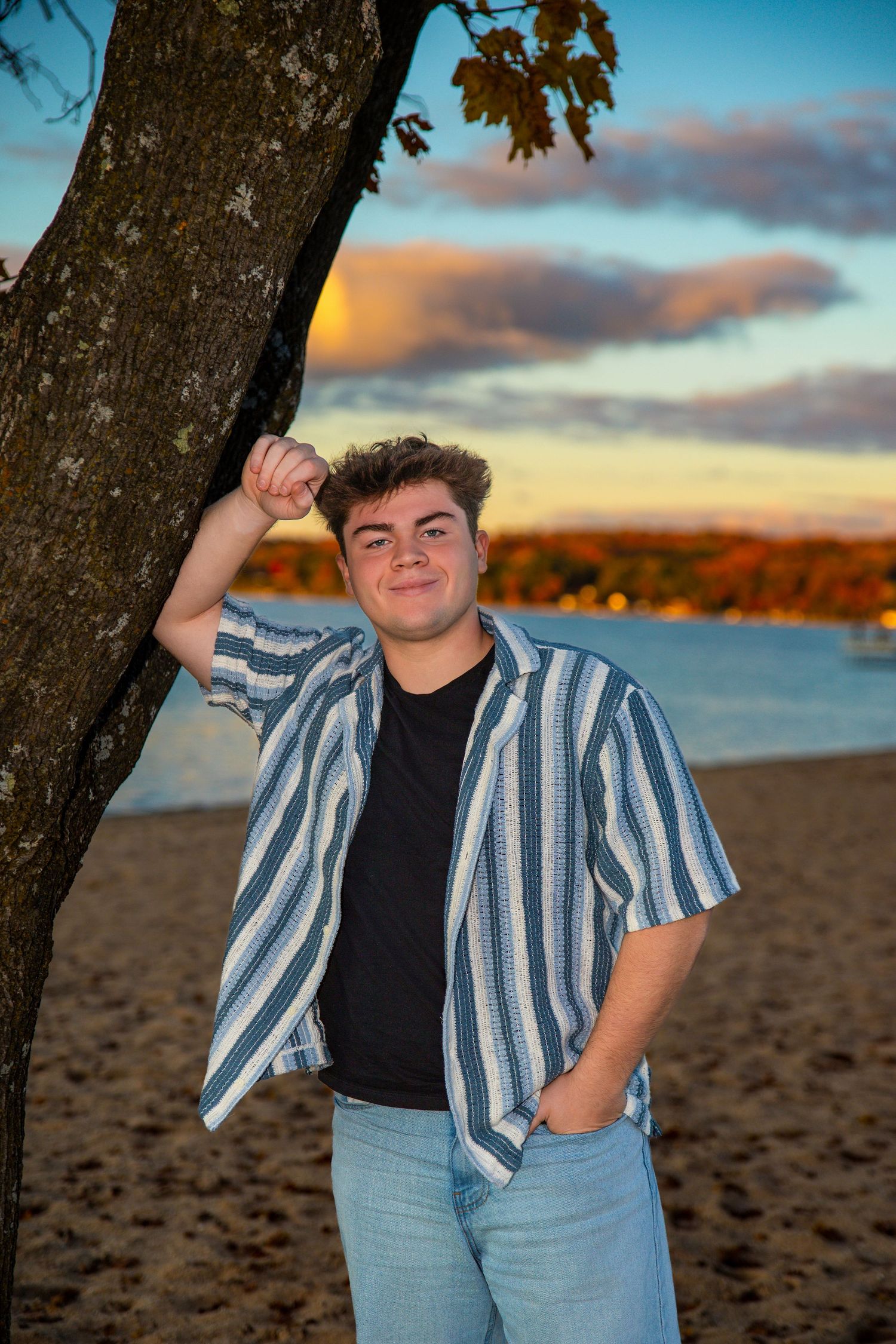 Person wearing striped shirt and jeans poses on beach at golden hour.