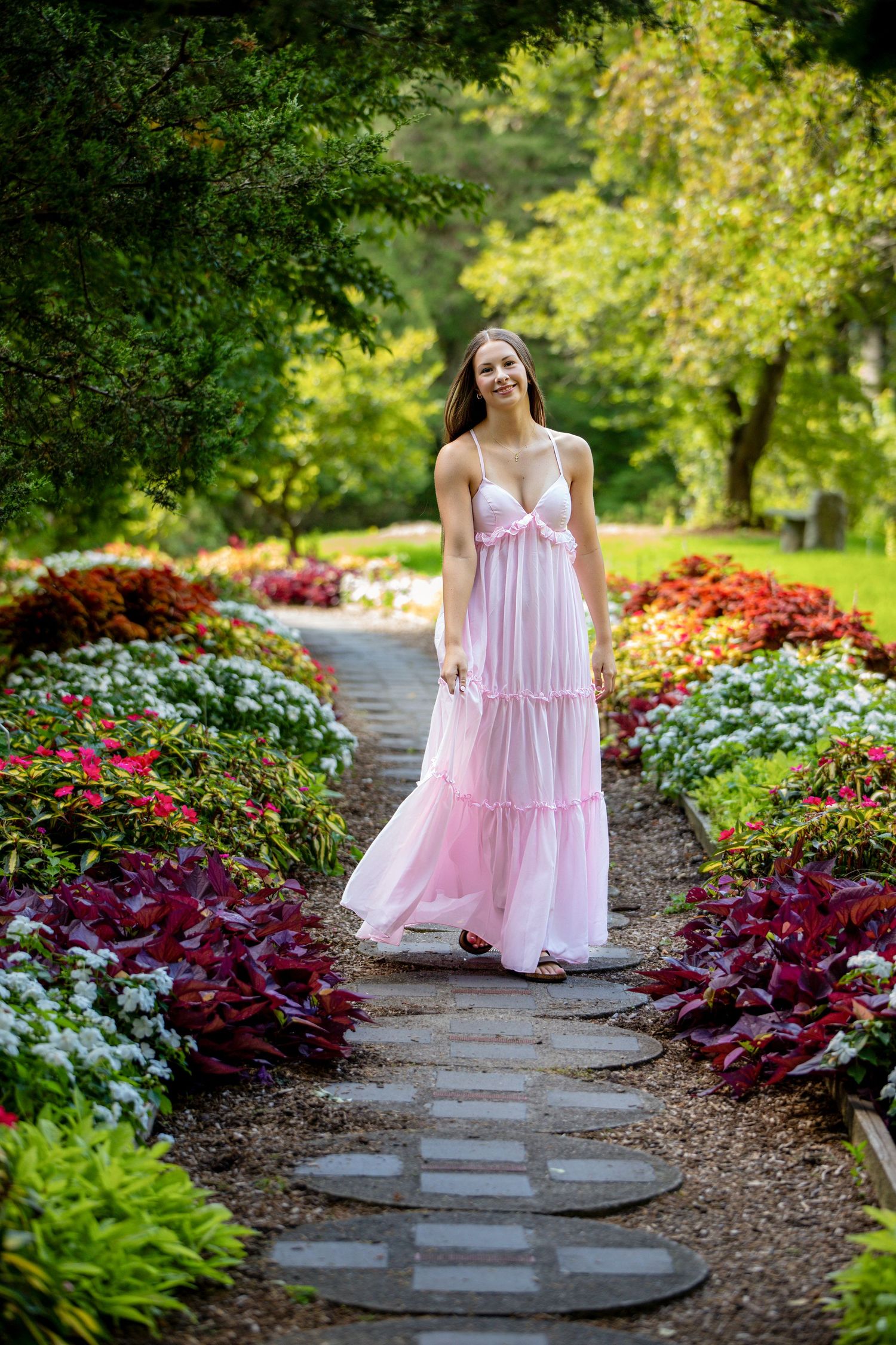A pink tiered dress stands out against colorful garden landscaping and stone path steps.