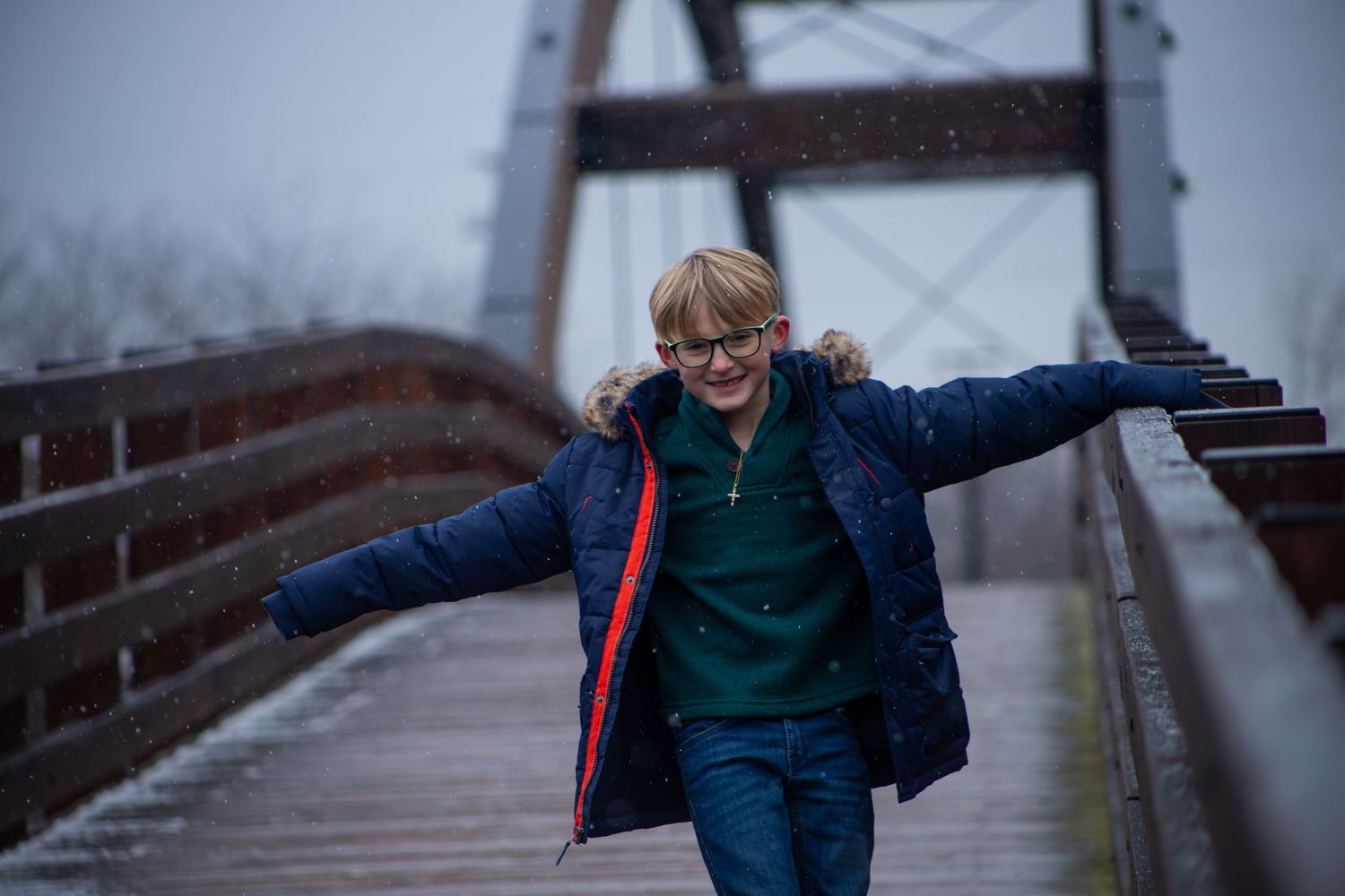 A joyful figure runs across a wooden bridge on a misty day with arms spread wide.