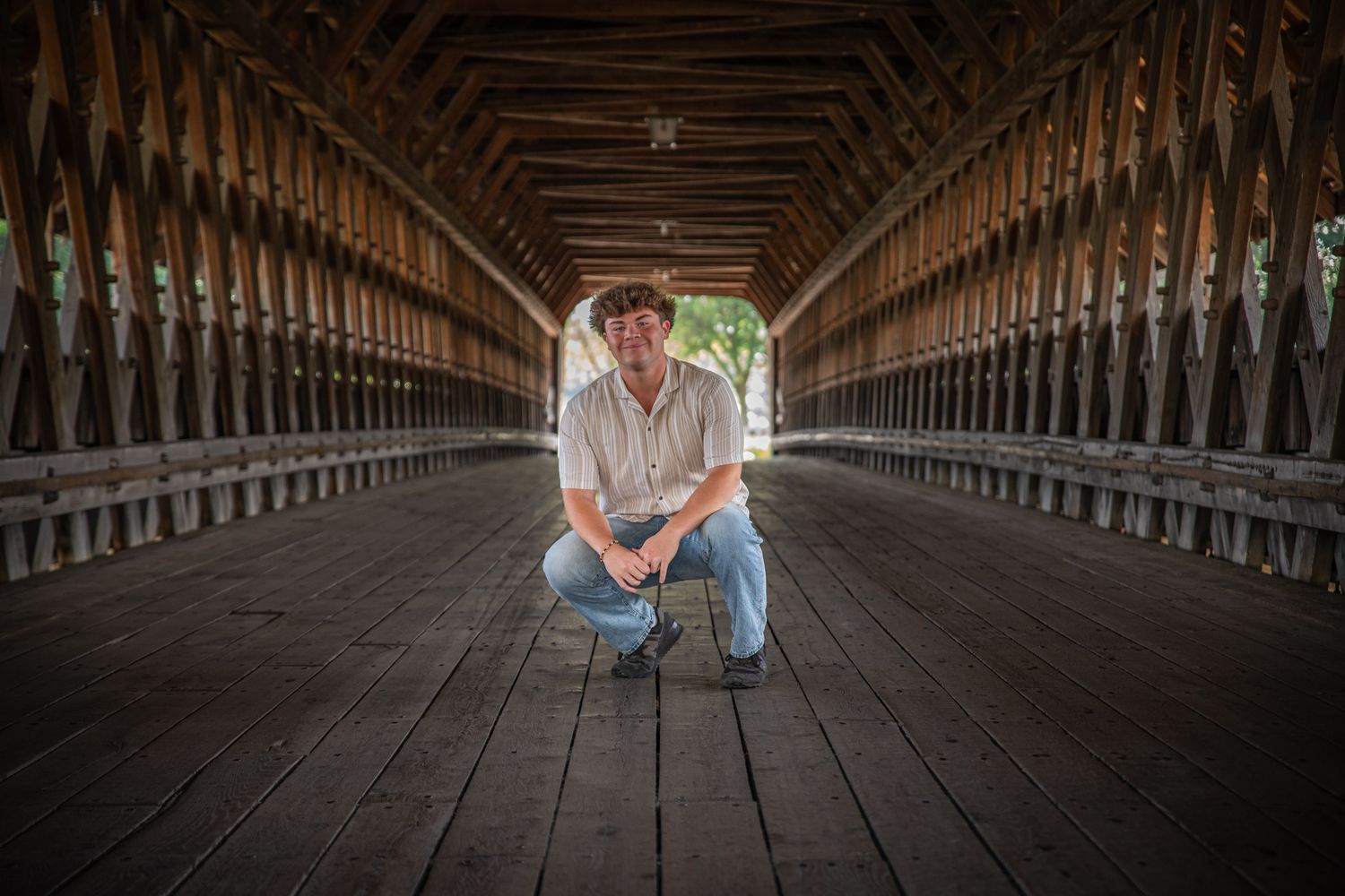 Person sitting on wooden floor inside covered bridge with dramatic lighting and architecture.
