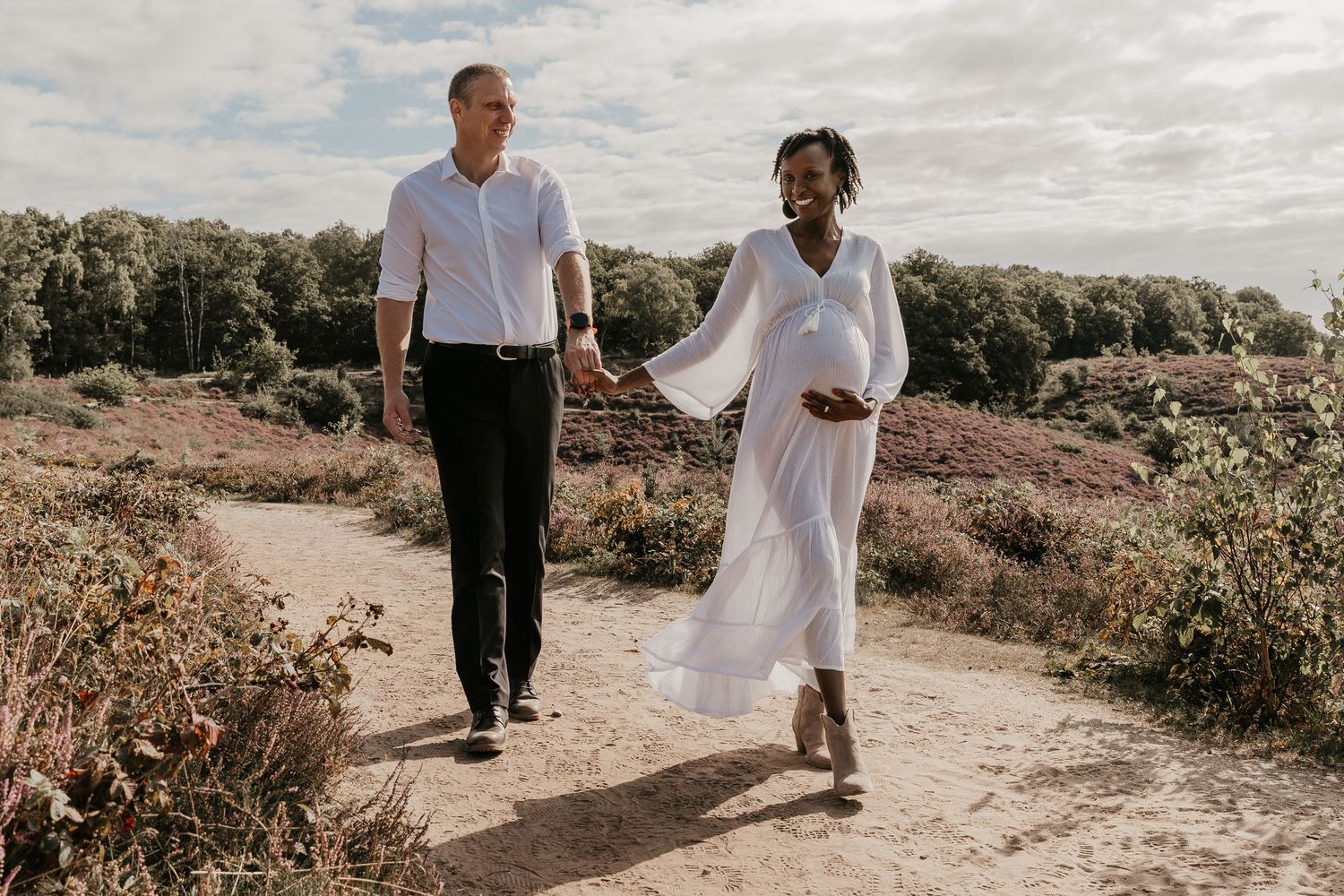 Een liefdevol moment tussen aanstaande ouders tijdens een zwangerschapsshoot op de Posbank, omringd door de paarse heide en de natuur.