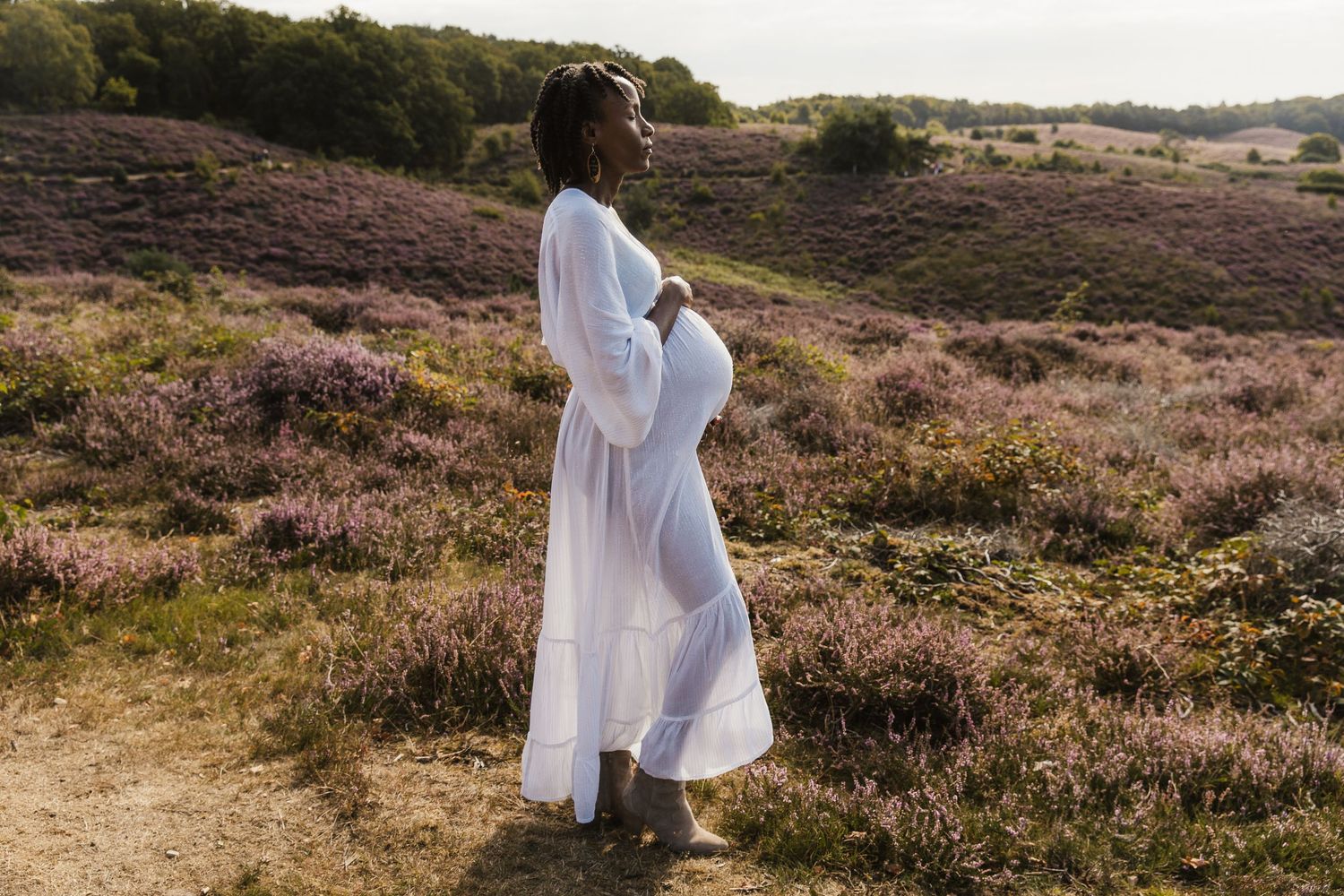 Een aanstaande mama straalt tijdens een liefdevolle zwangerschapsshoot op de Posbank, omringd door de paarse heide en de prachtige natuur.