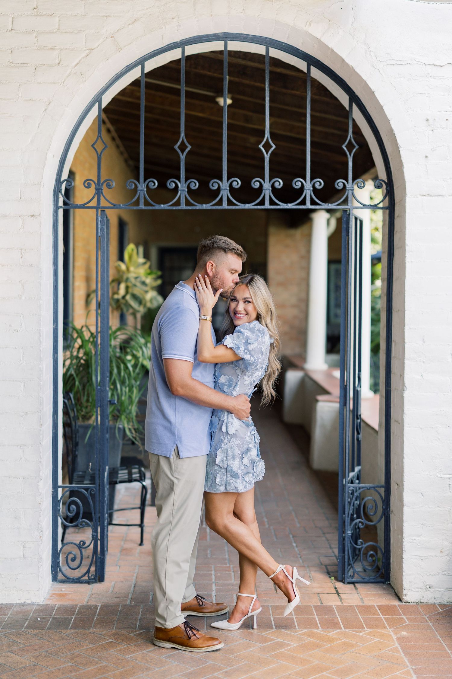 Couple embracing and kissing under an ornate iron archway at a romantic outdoor venue.