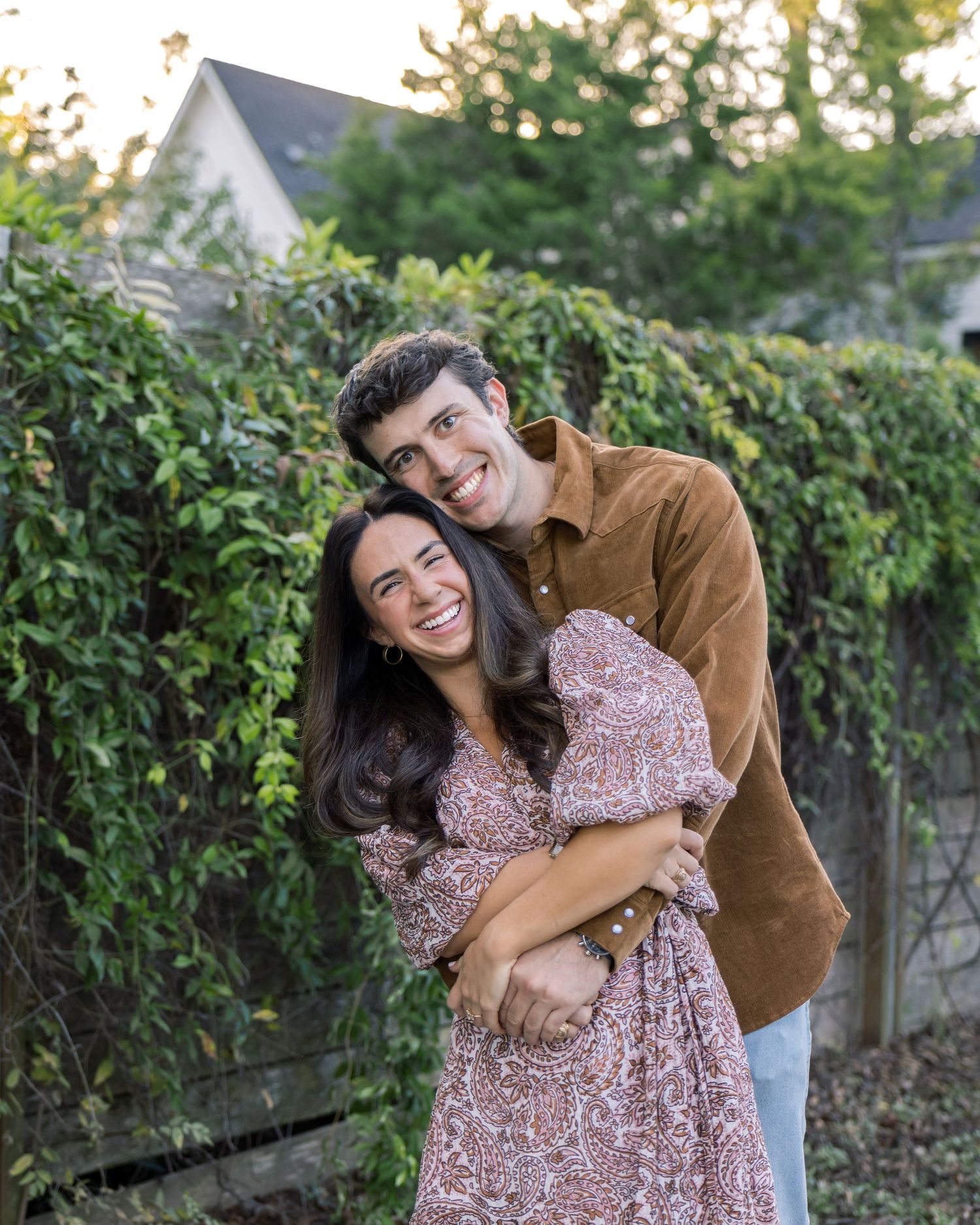 Couple hugging and laughing in front of a lush ivy wall during golden hour in autumn.