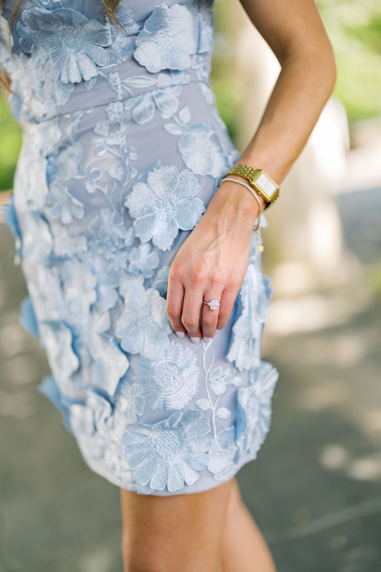 Woman wearing a light blue floral applique mini dress with gold watch and diamond ring.