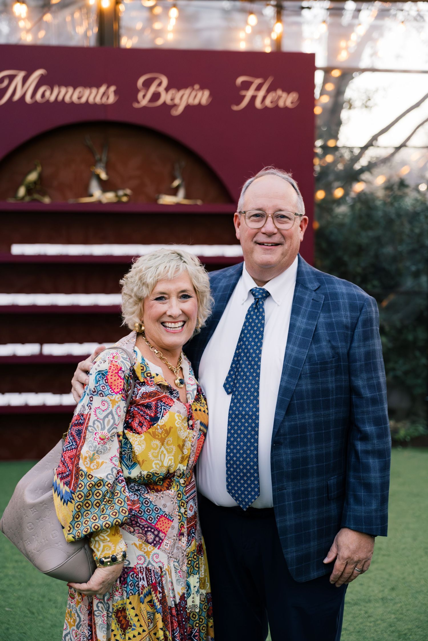 Smiling couple posing outdoors at an event venue with a 'Moments Begin Here' sign backdrop.