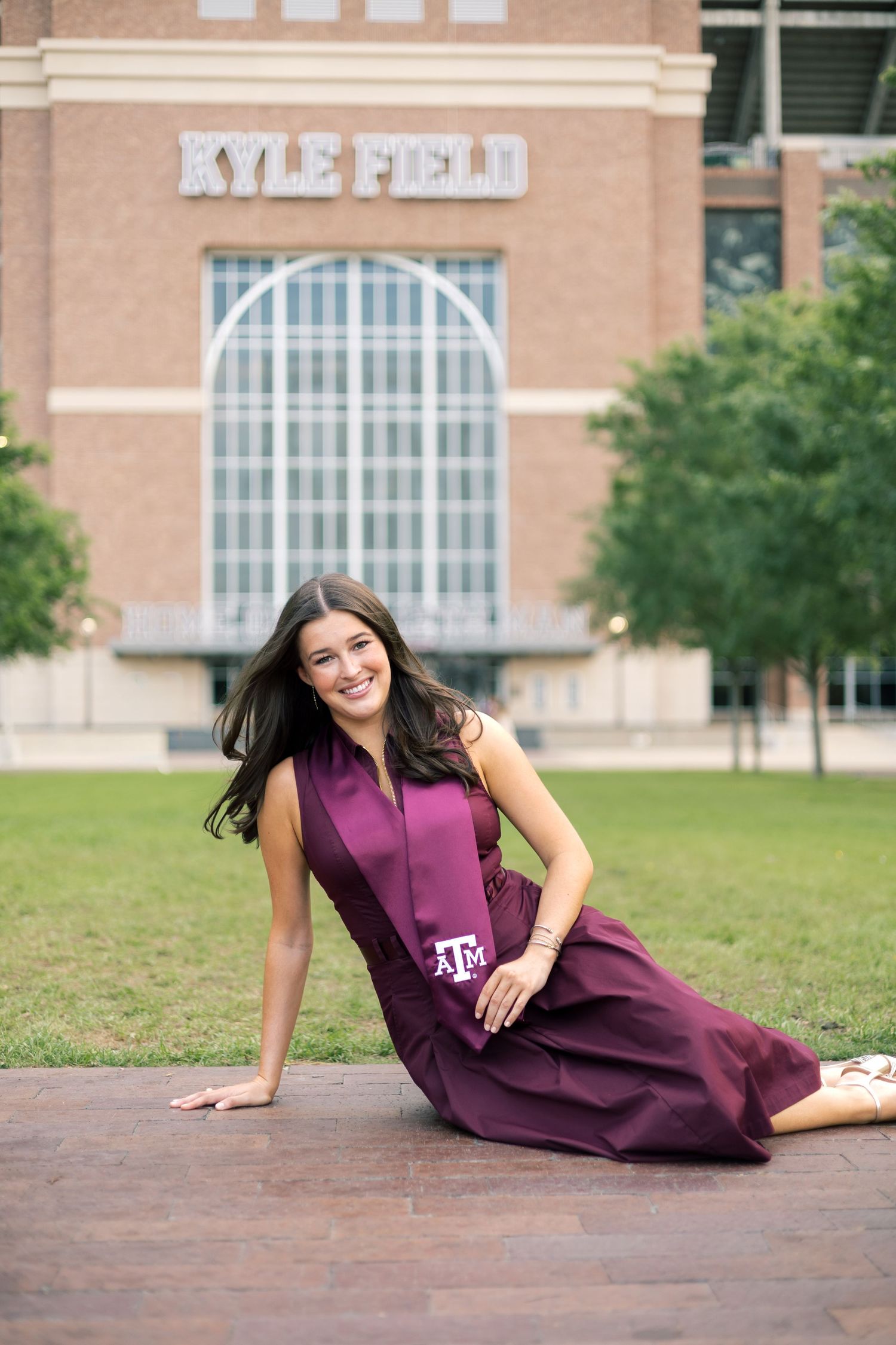 Texas A&M graduate in maroon stole poses playfully on brick path at Kyle Field.