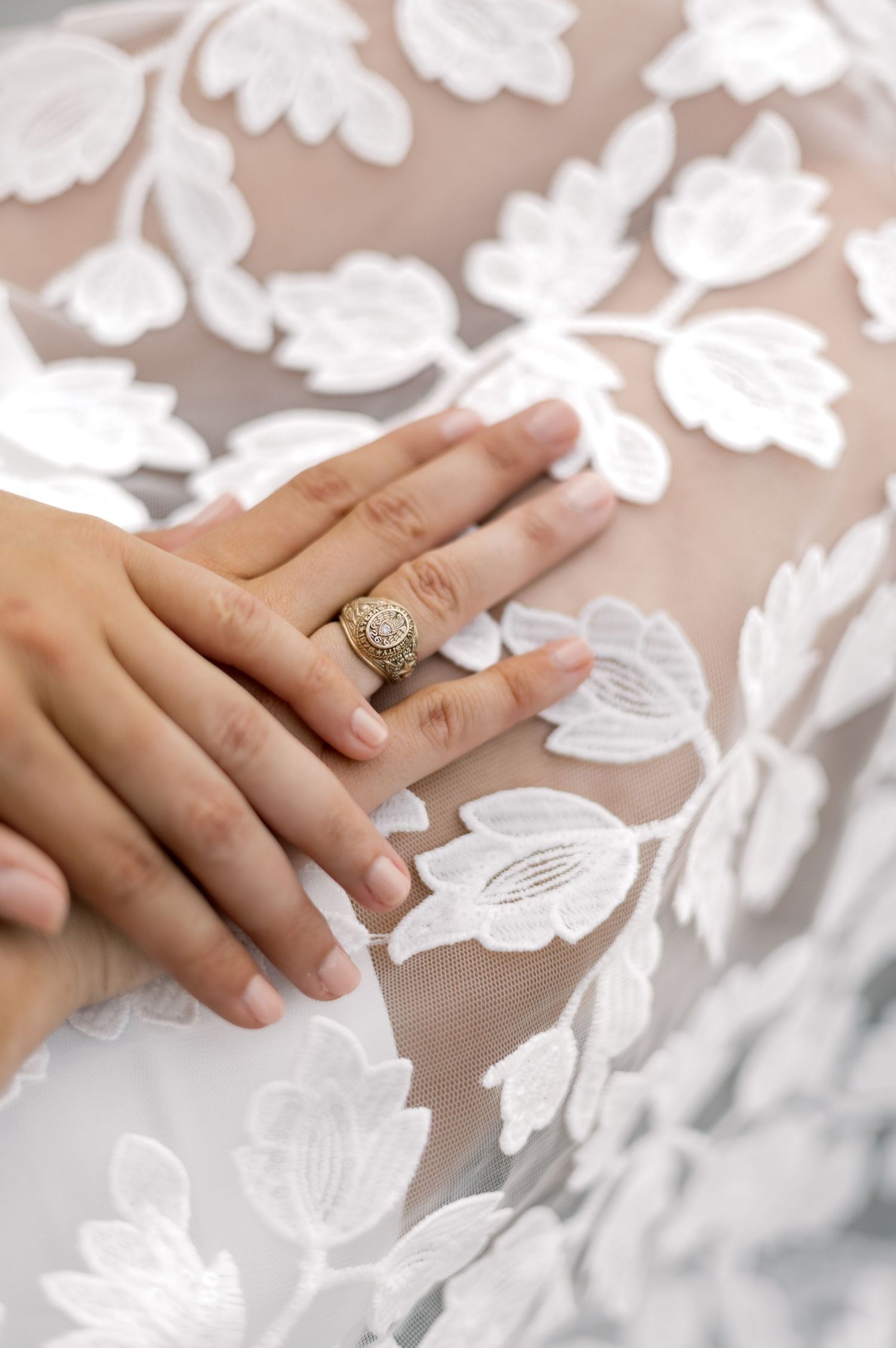 Close-up of hands with gold ring resting on white floral embroidered lace fabric.