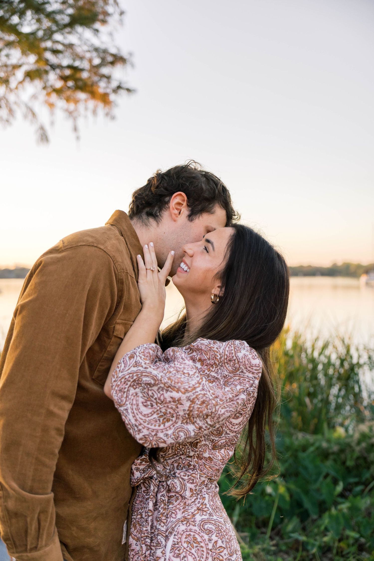 Couple sharing a tender kiss near a peaceful lake at golden hour sunset outdoors.
