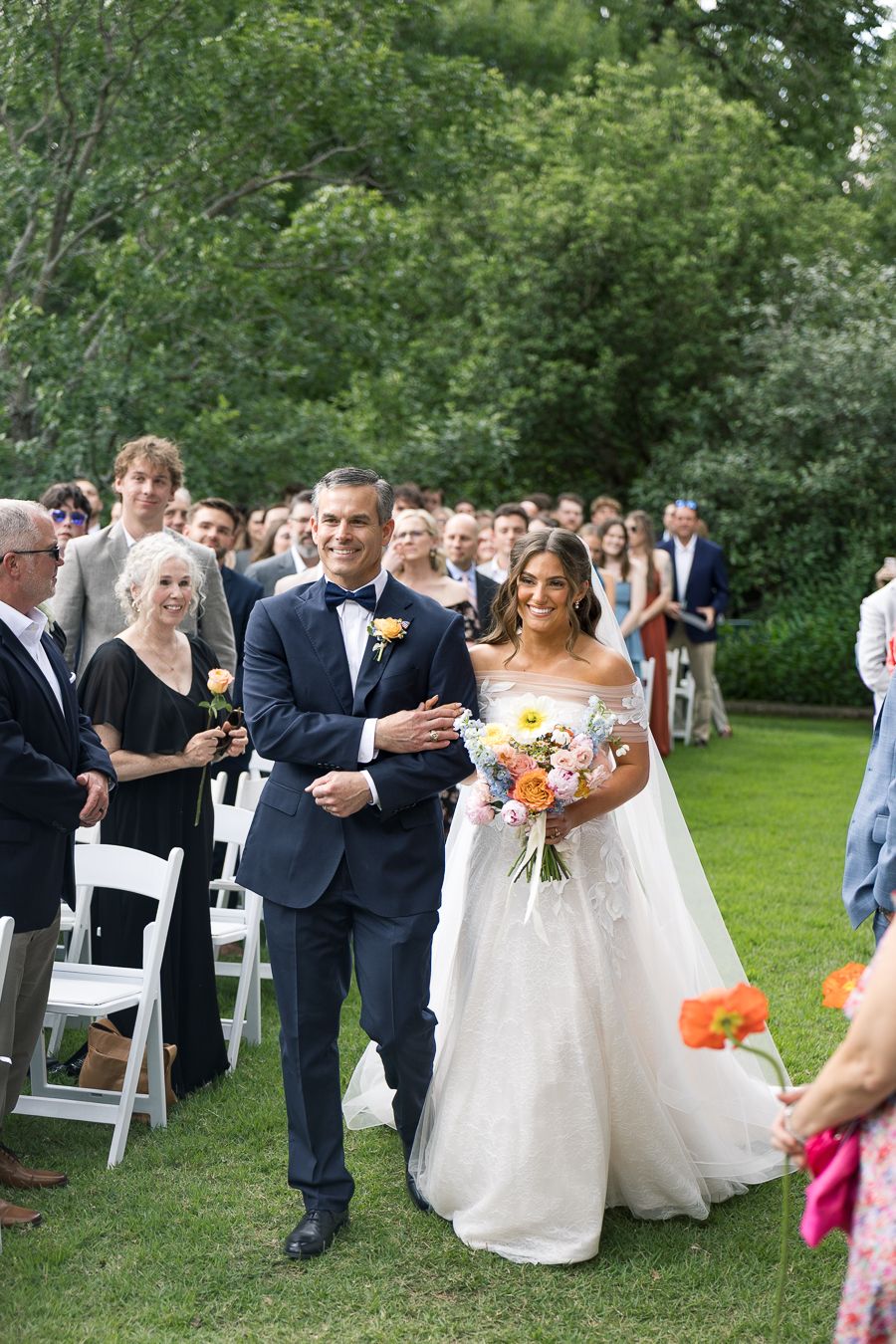 Bride and groom walk down the aisle at an outdoor garden wedding ceremony, surrounded by smiling guests.