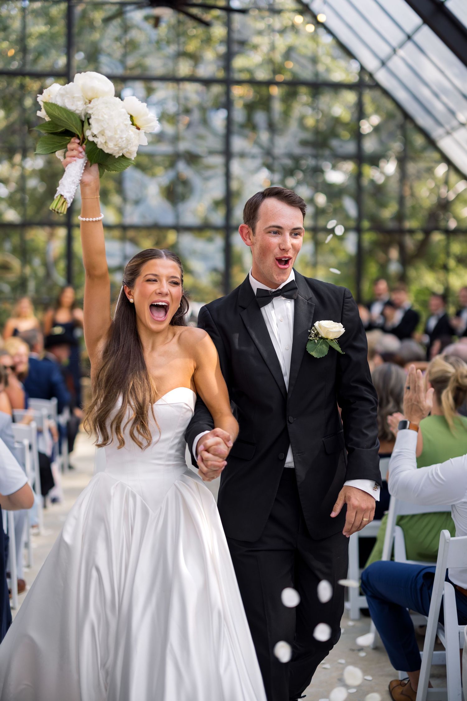 Joyful bride and groom walk down the aisle after wedding ceremony in a greenhouse venue.