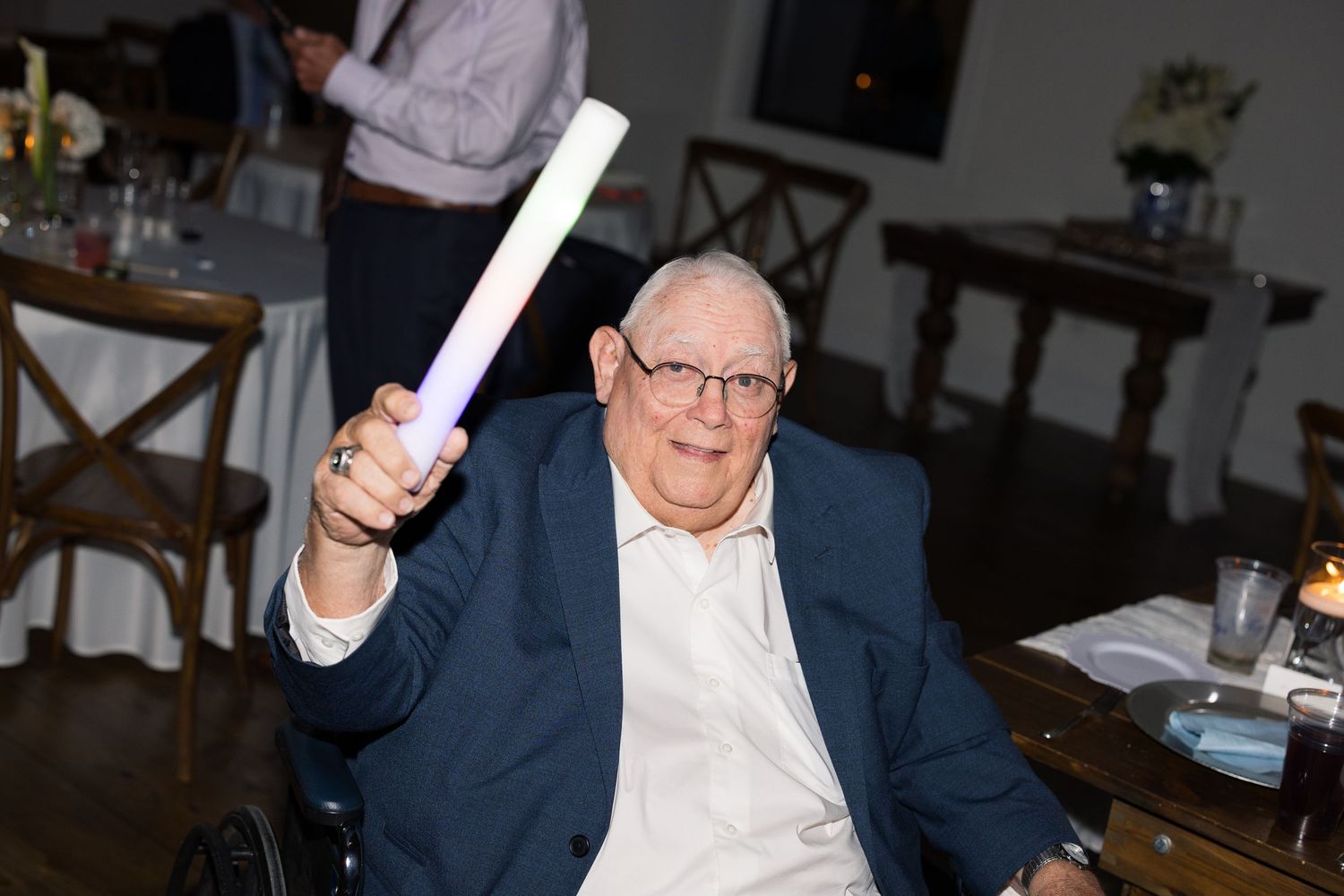 Elderly man smiling and holding a glow stick at an indoor celebration event.