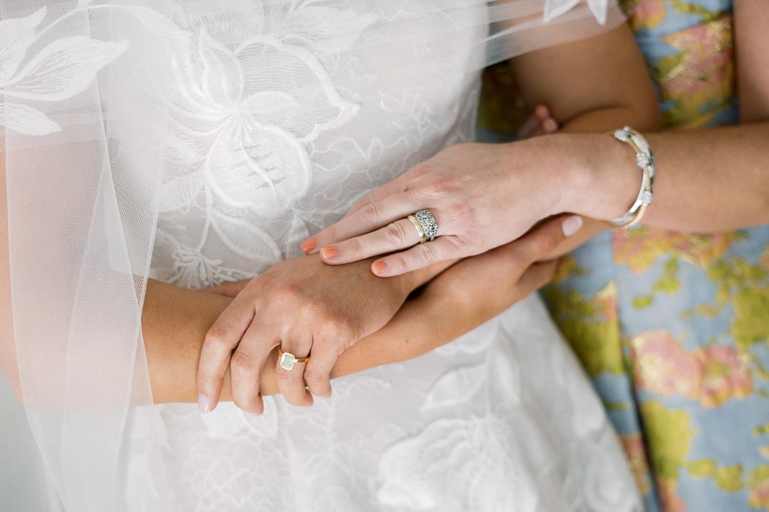 Close-up of bride and mother hands showing wedding rings, engagement ring, and bracelet on wedding day.