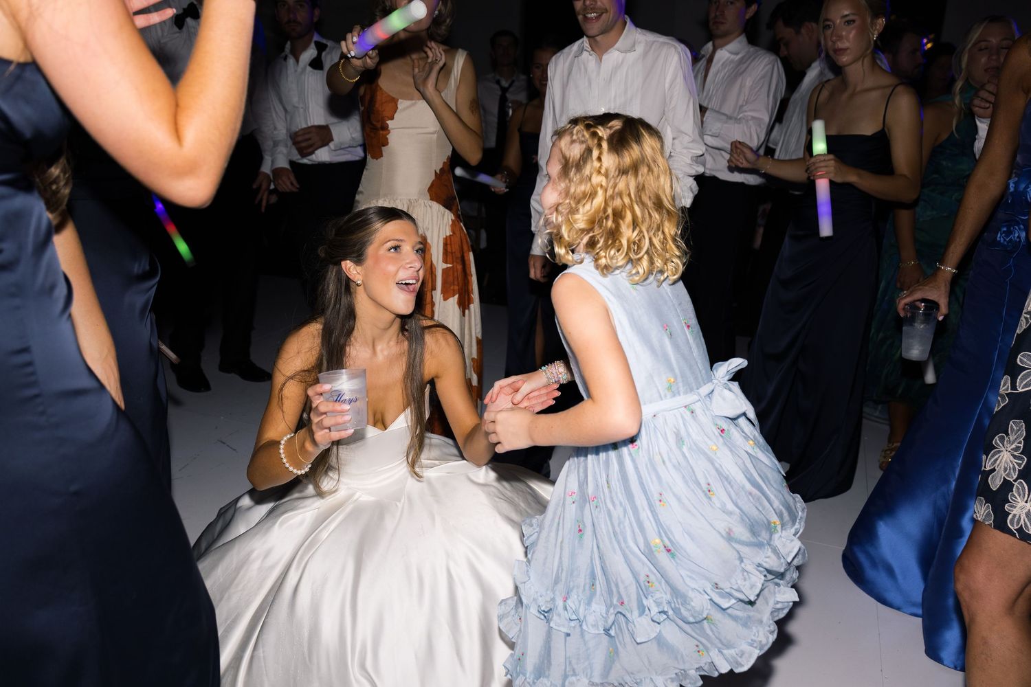 Two women in elegant gowns dancing joyfully at a formal event or wedding reception.