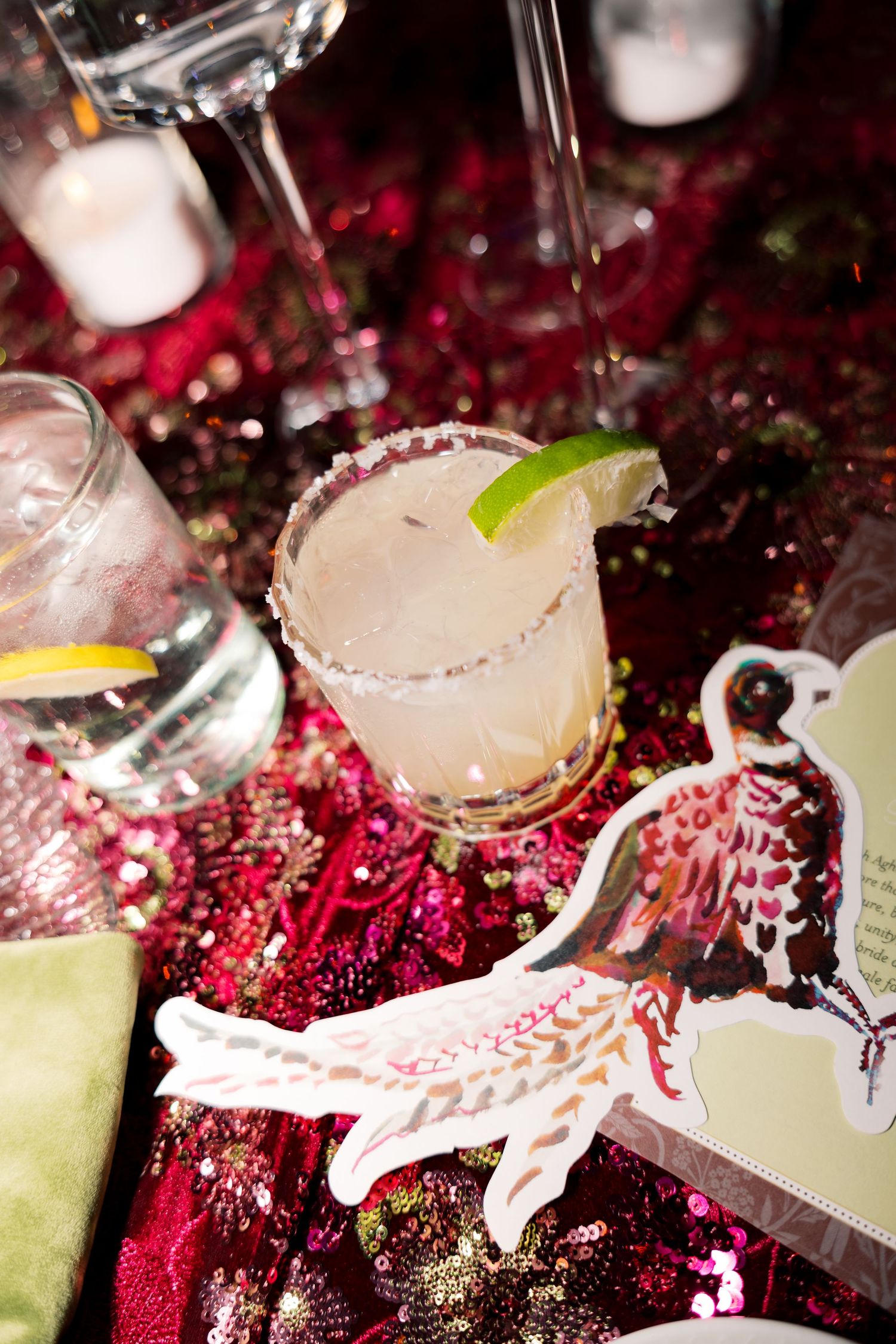 Margarita cocktail with salted rim and lime garnish on a sparkly red sequin tablecloth at a festive party.
