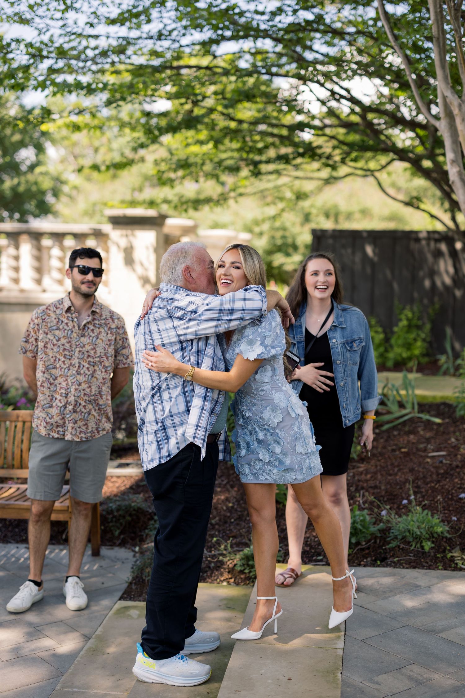 Family group hugging and smiling outdoors in a garden patio setting during a sunny day celebration.
