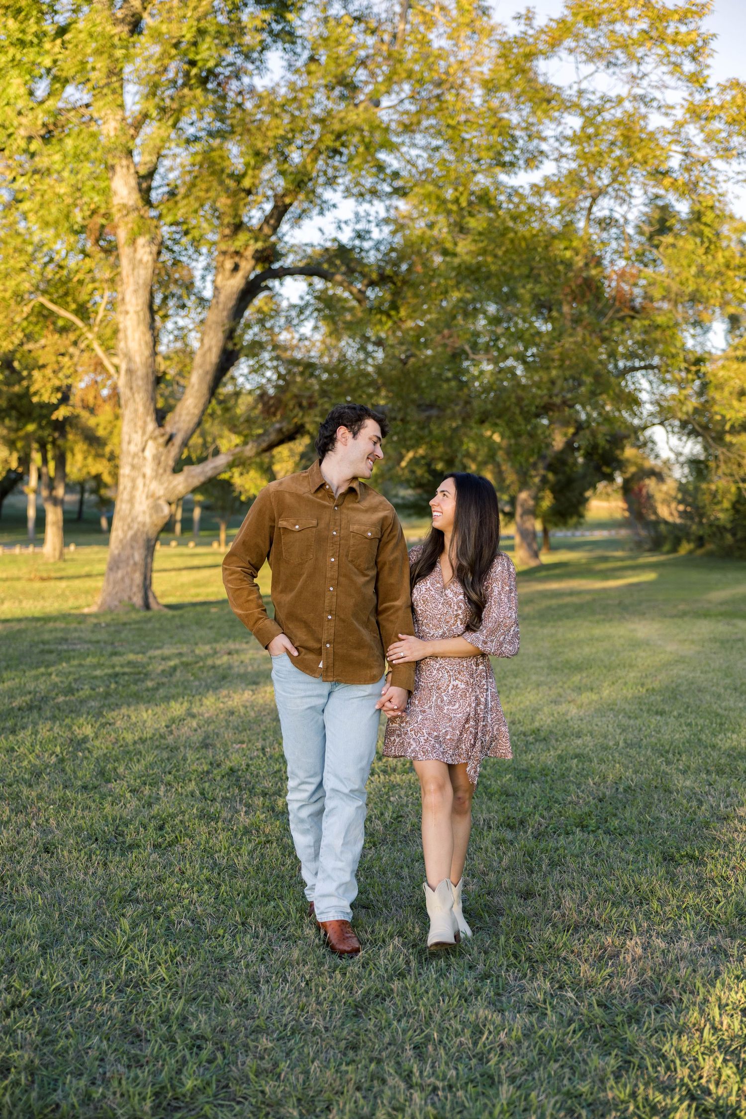 Happy couple walking hand in hand through a lush green park during golden hour sunset.
