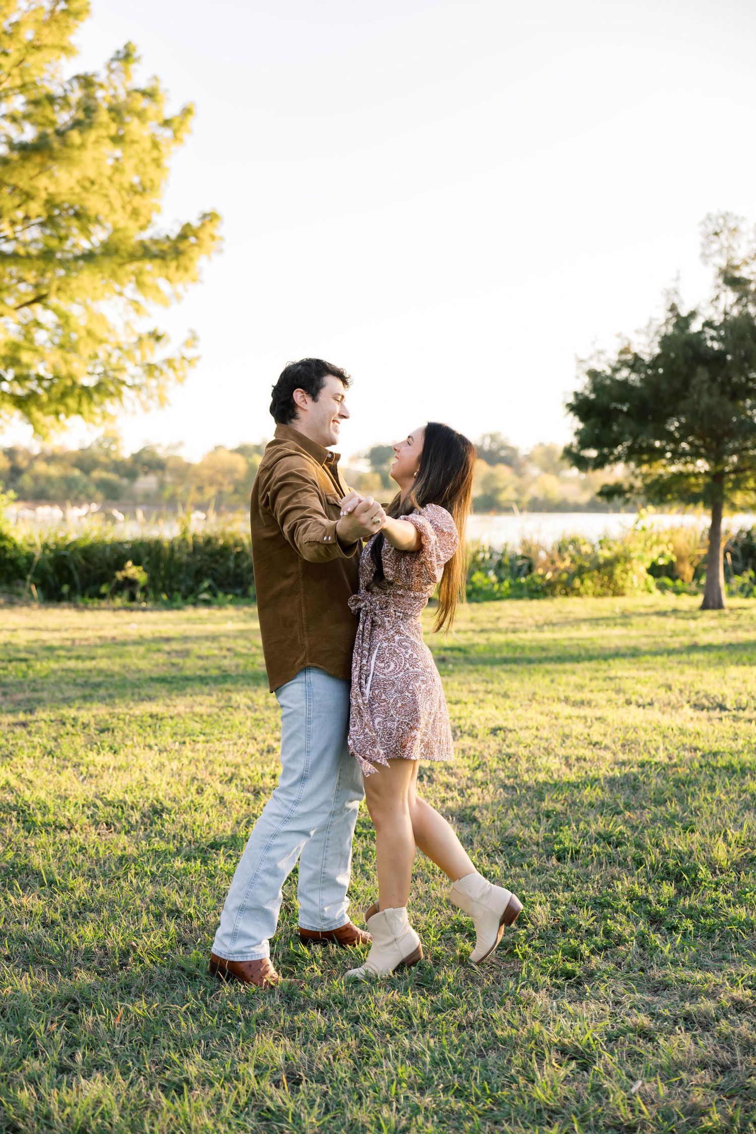 Romantic couple dancing together on green grass in a sunlit park near a lake.