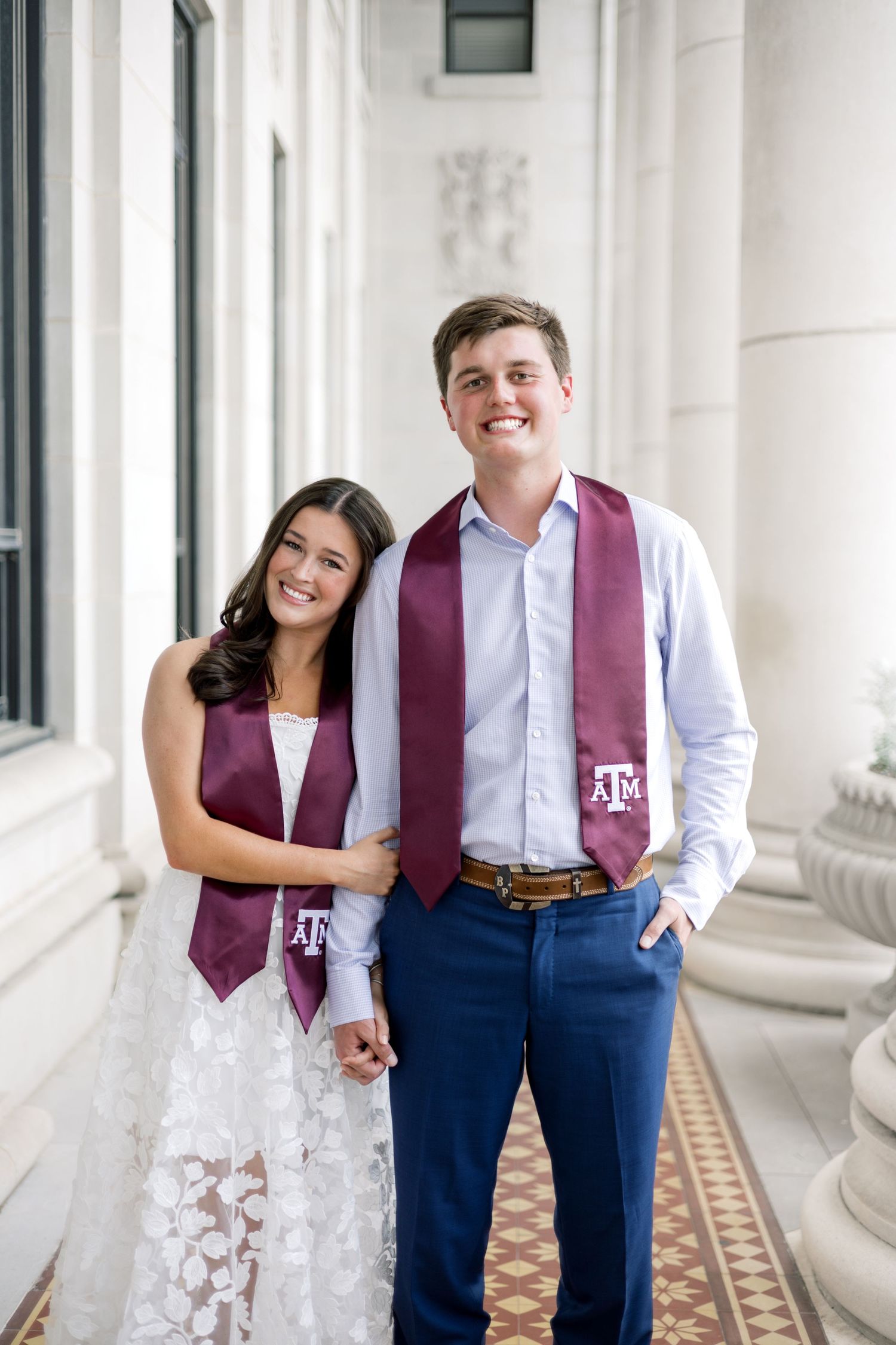 Young man and woman posing together in Texas A&M graduation stoles, smiling in a classic columned architectural setting.