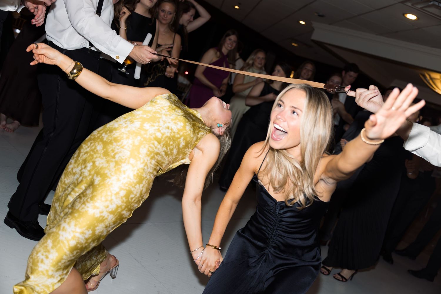 Guests doing the limbo dance at a lively wedding reception party on a white dance floor.