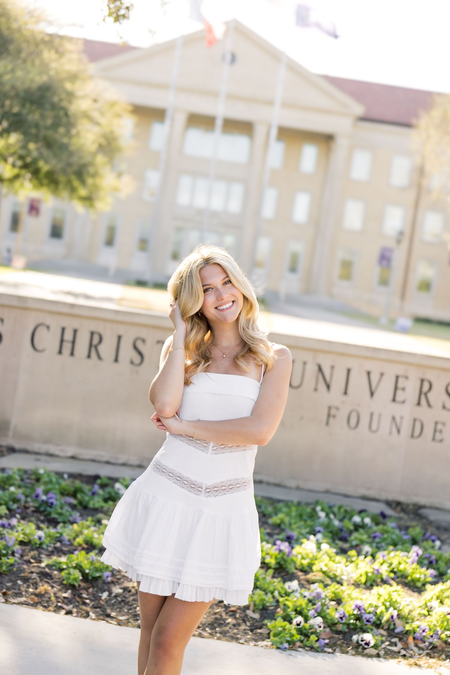 Smiling blonde woman in white strapless dress standing before Texas Christian University Founders sign.