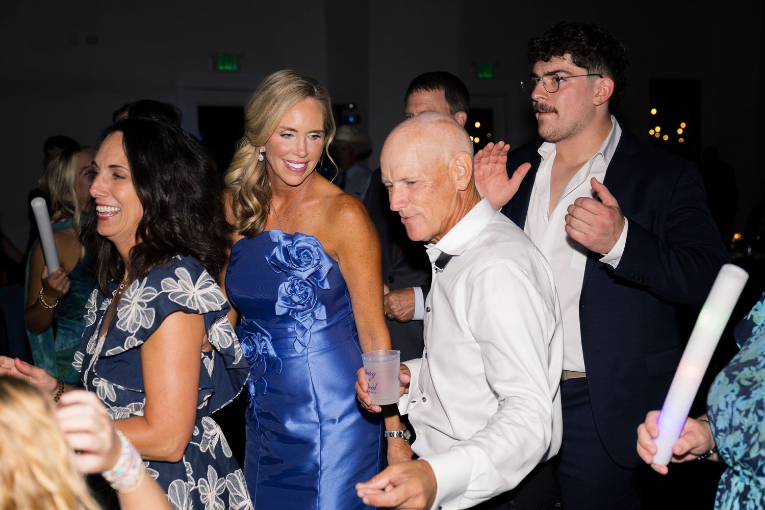Guests dancing joyfully at an elegant wedding reception, including a woman in a blue strapless gown.