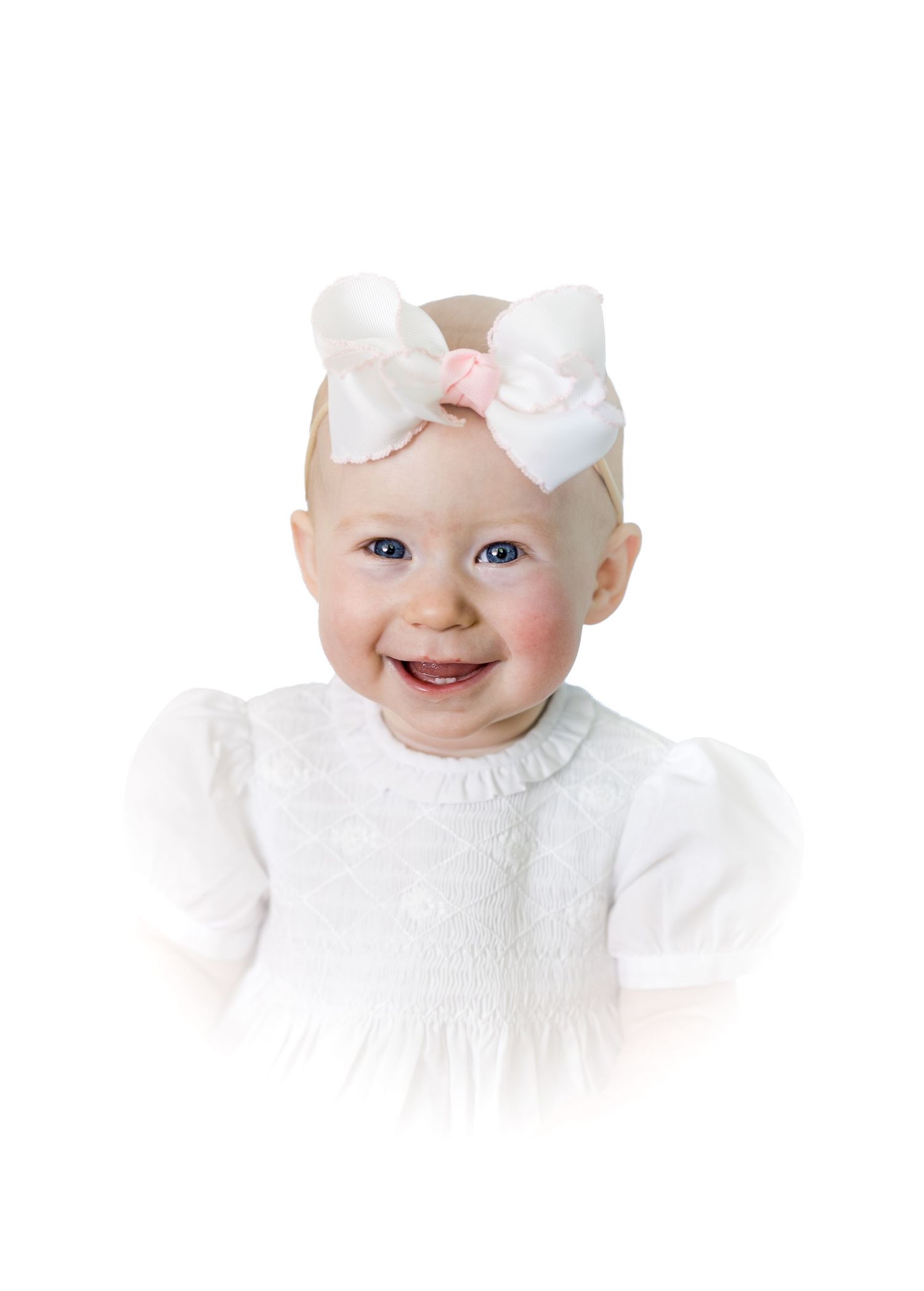 Smiling baby girl wearing a white dress and bow headband on a white background.