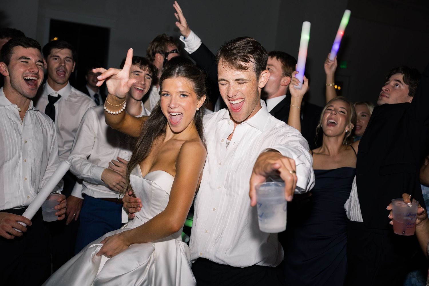 Bride and groom dancing joyfully with guests at a lively wedding reception party.