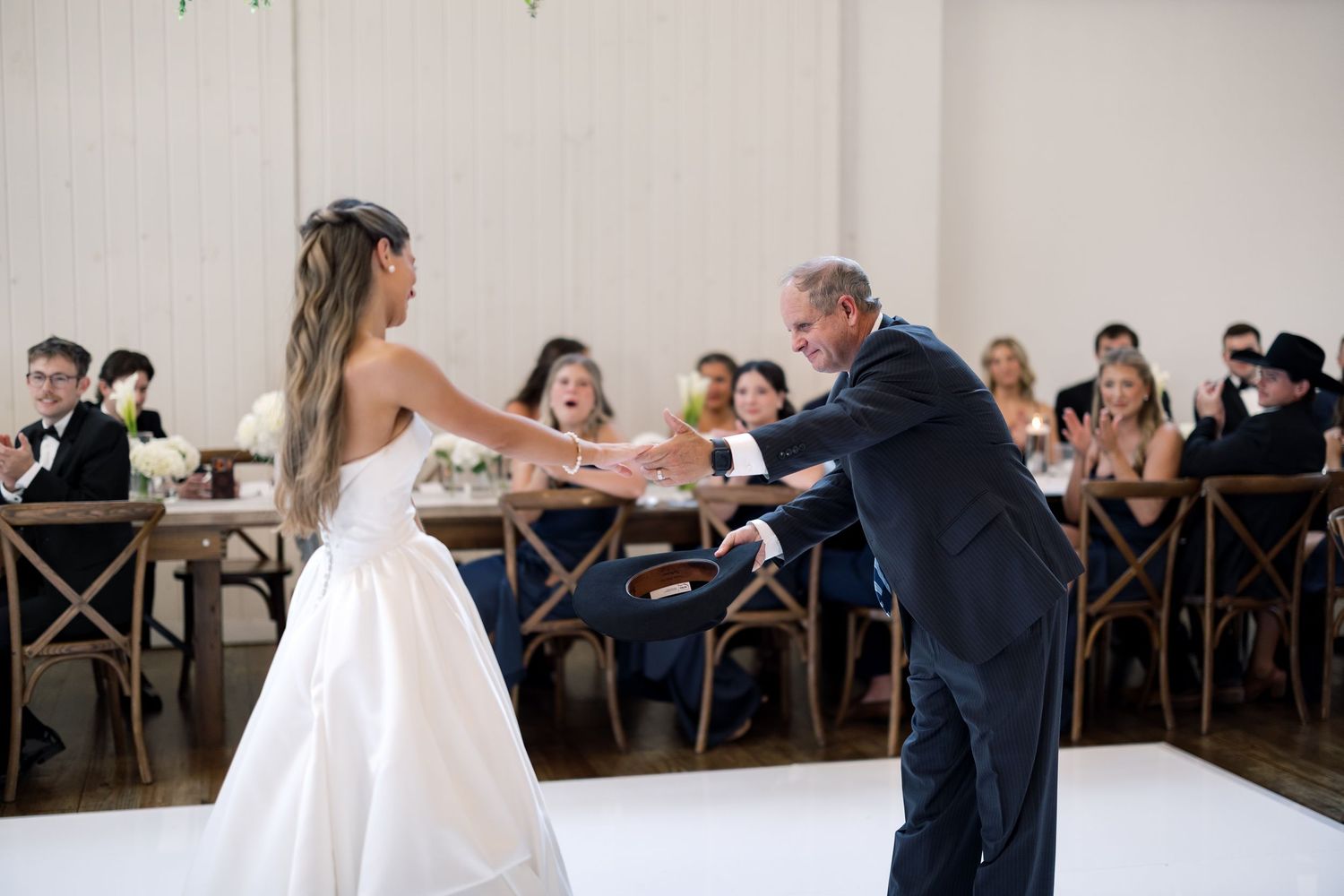 Bride and father share an emotional first dance at elegant wedding reception with guests watching in background.