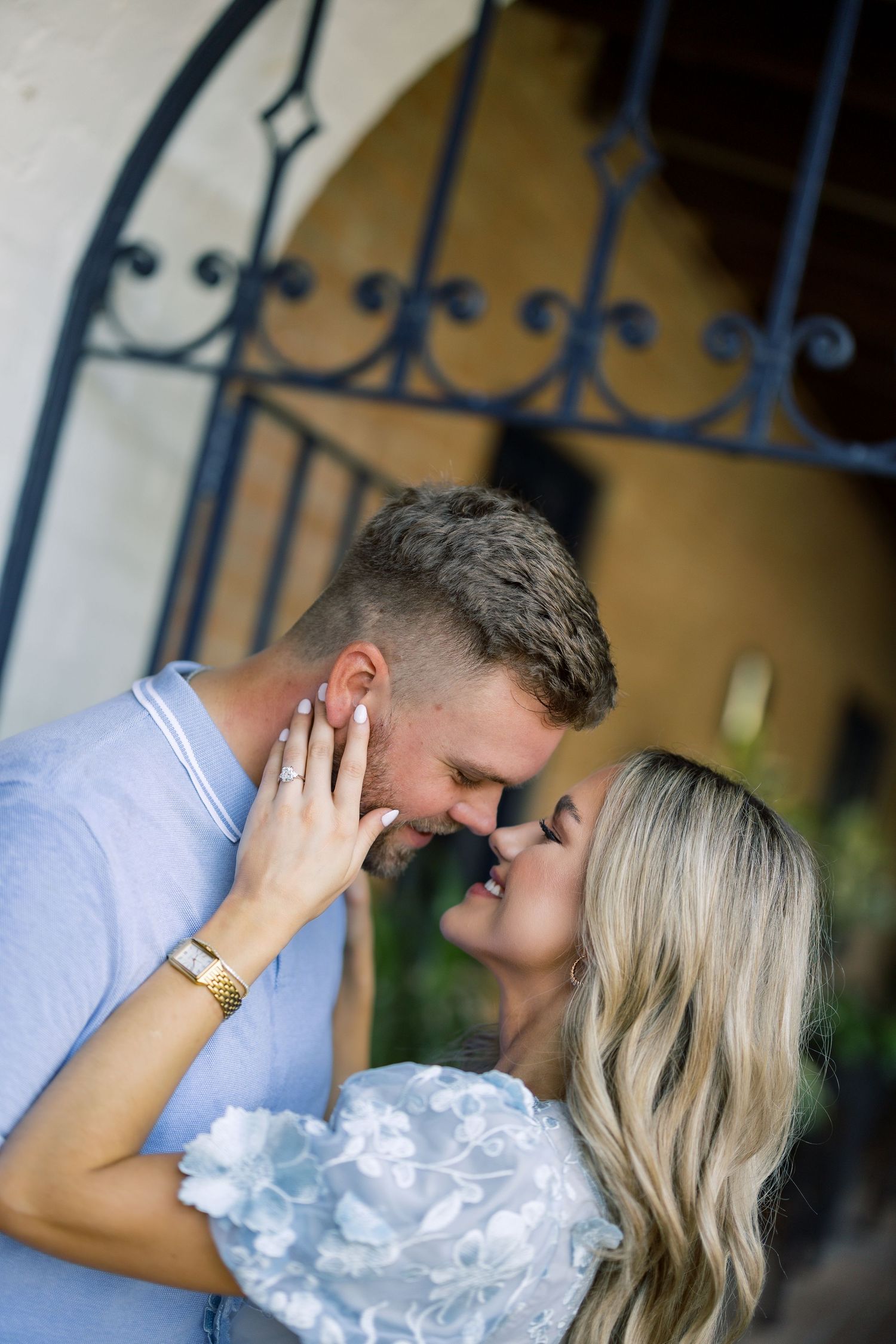 A couple shares a romantic moment, almost kissing, as the woman shows off her engagement ring outdoors.