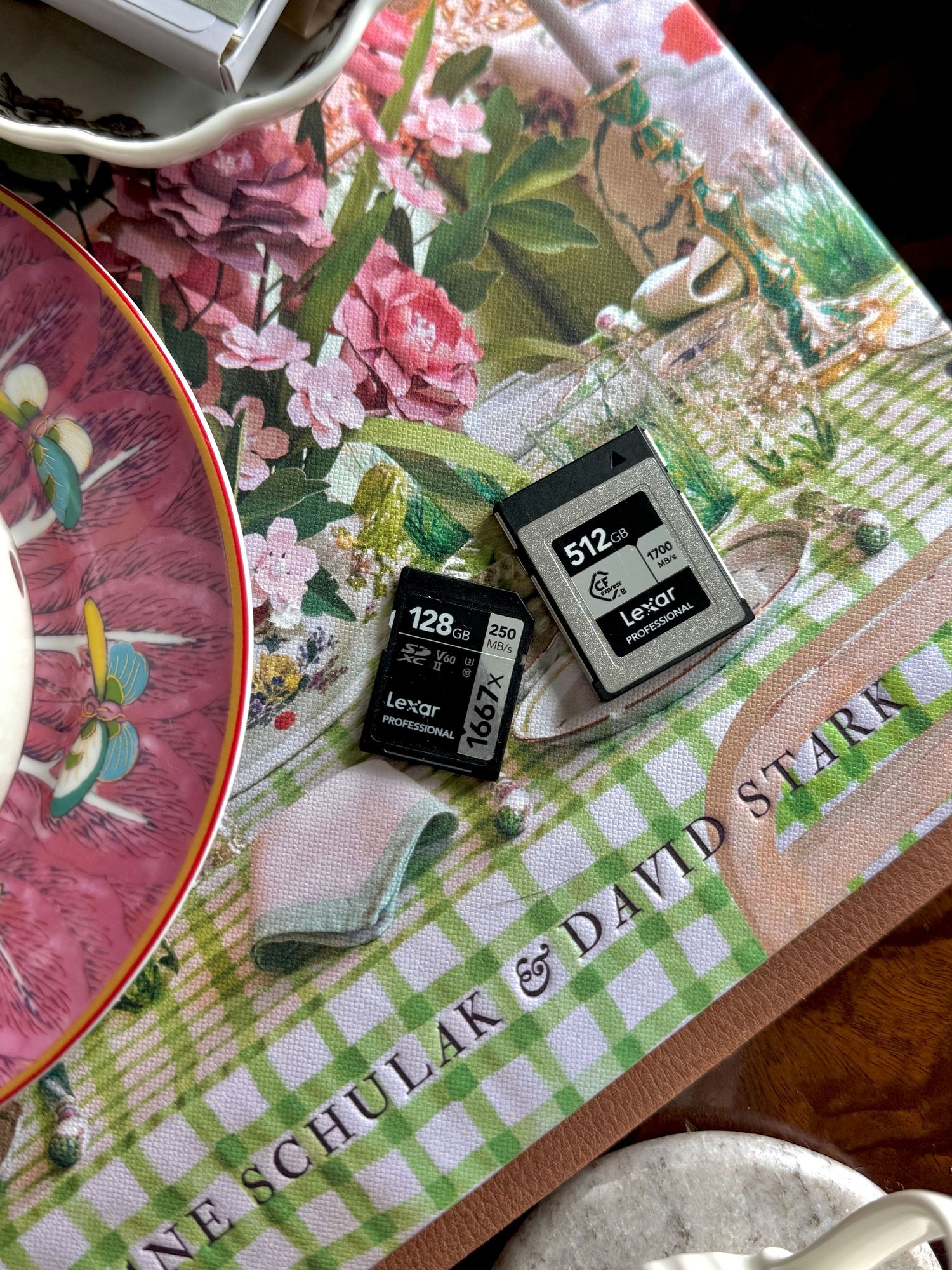 Two Lexar memory cards, 128GB and 512GB, on a floral green gingham tablecloth with a David Stark design.