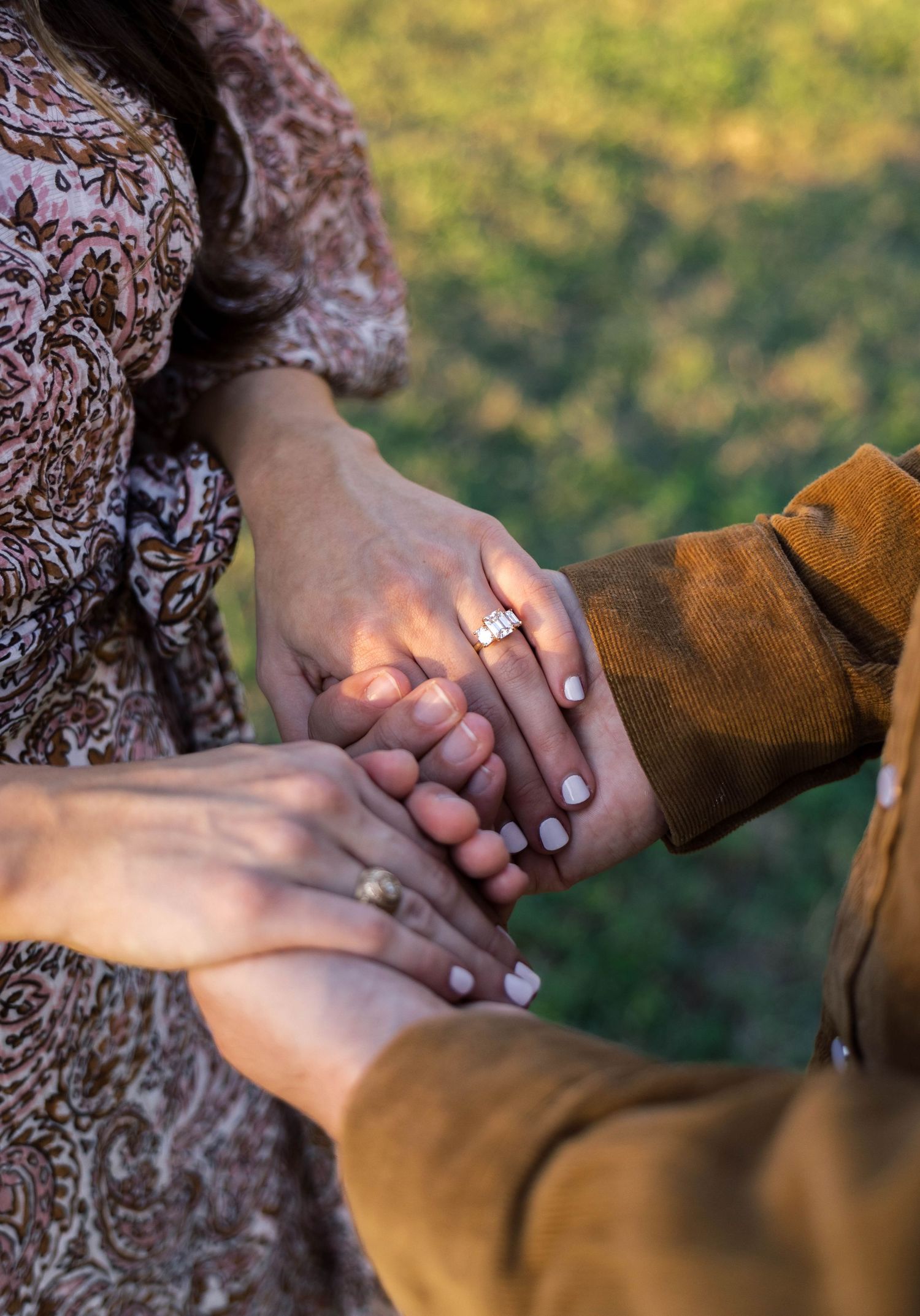 Close-up of engaged couple holding hands showing a sparkling diamond engagement ring outdoors.