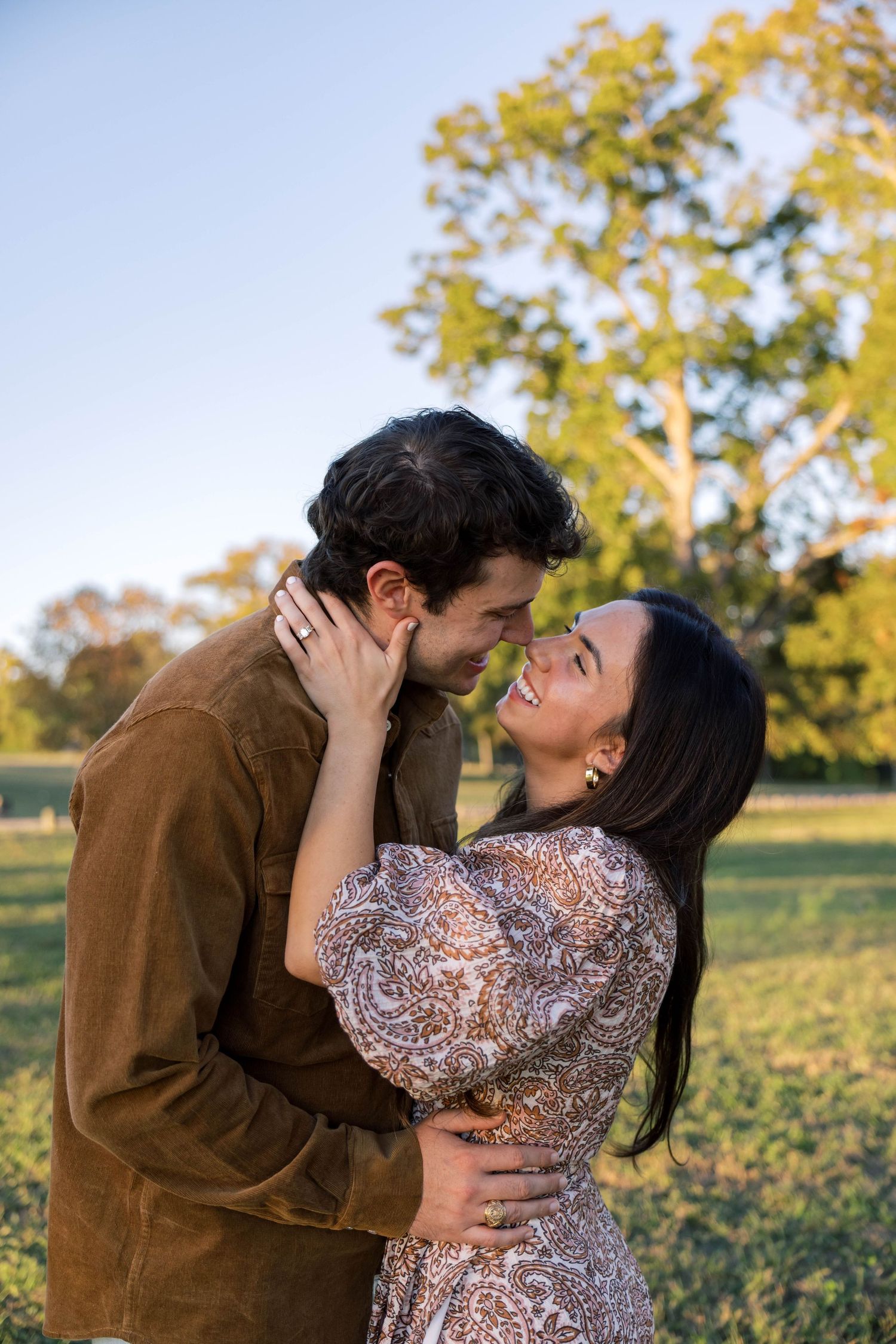 Smiling couple embracing and about to kiss in a beautiful outdoor park at sunset.