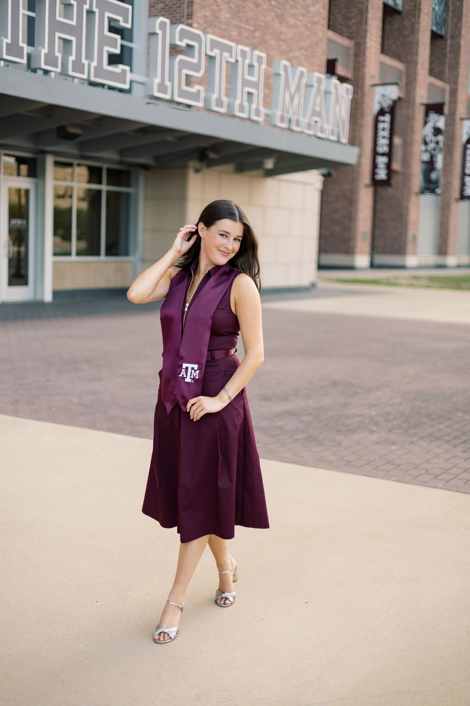 Elegant Texas A&M graduate in maroon dress with stole posing at The 12th Man stadium entrance.