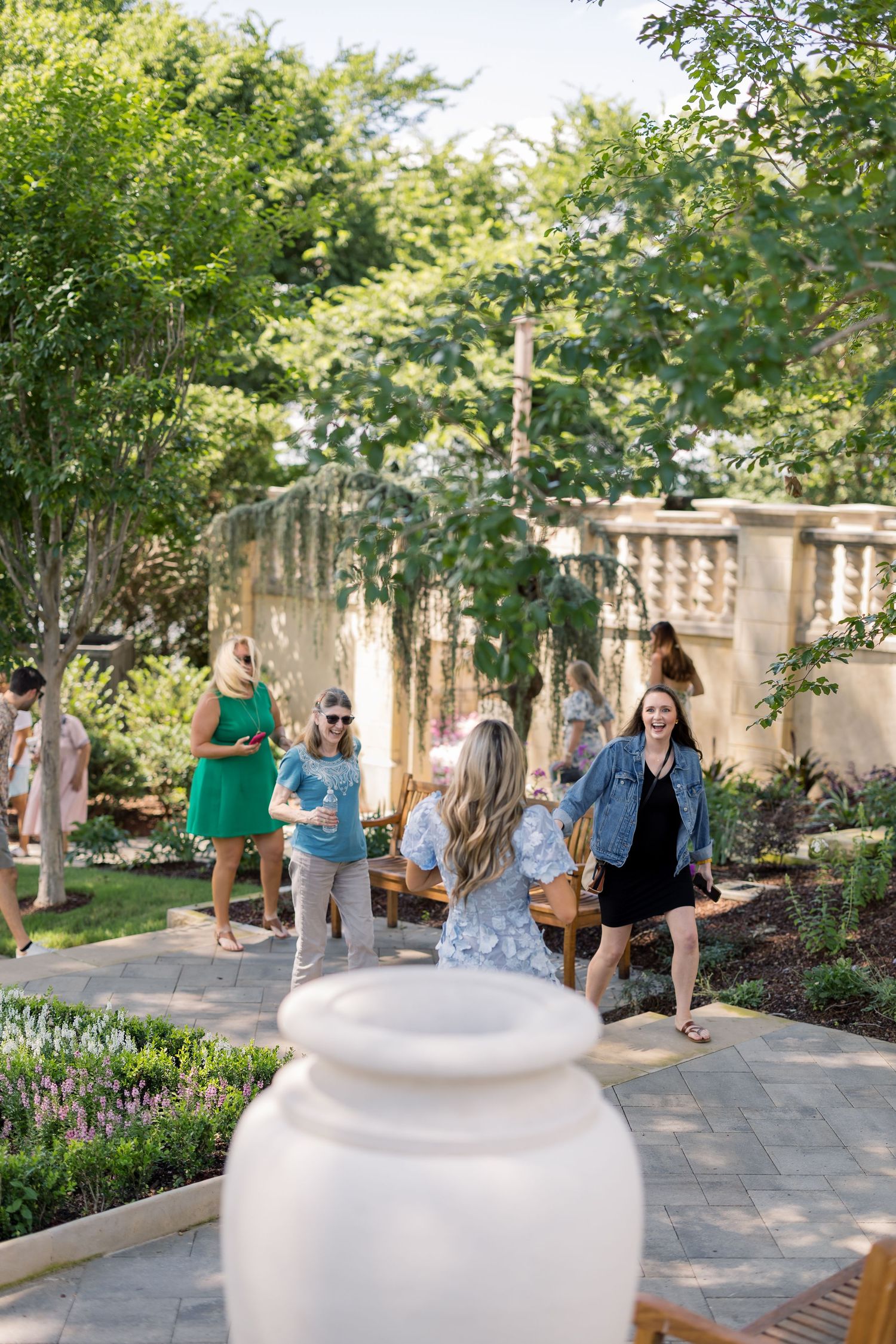 Guests socializing in a beautiful outdoor garden patio with lush greenery and stone walls at a summer event.