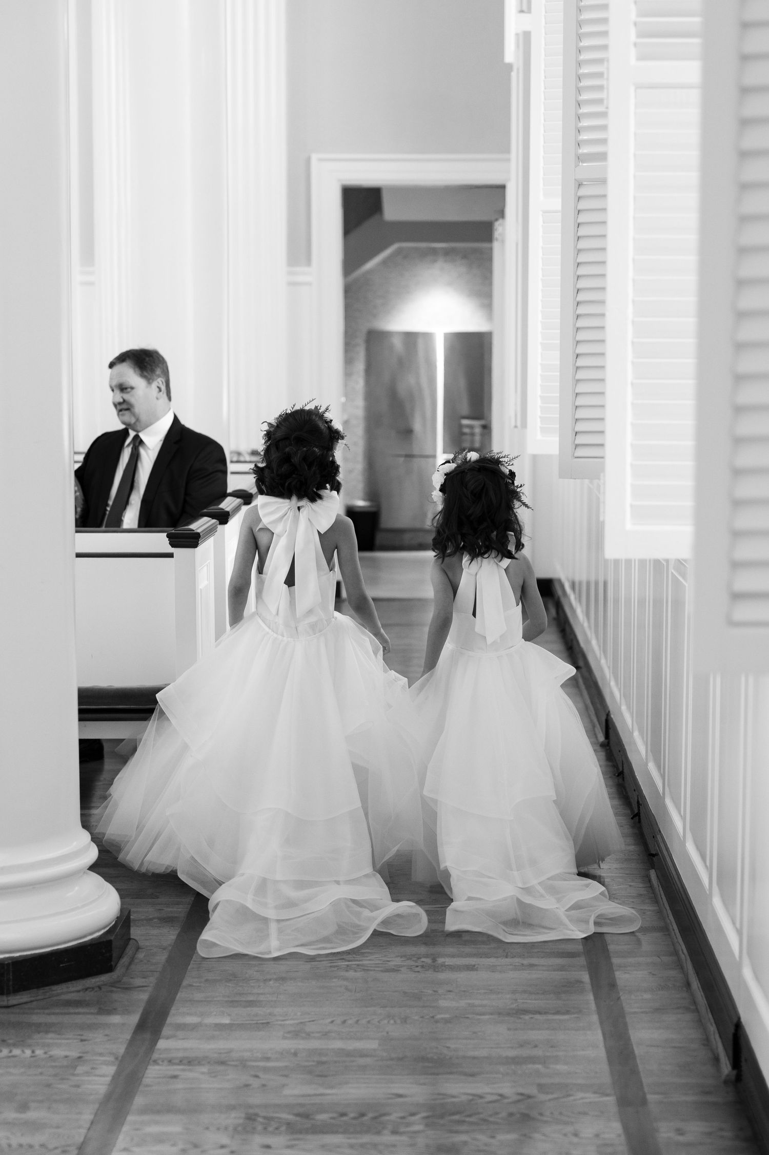Two flower girls in white tulle dresses walk down a church aisle during a wedding ceremony.