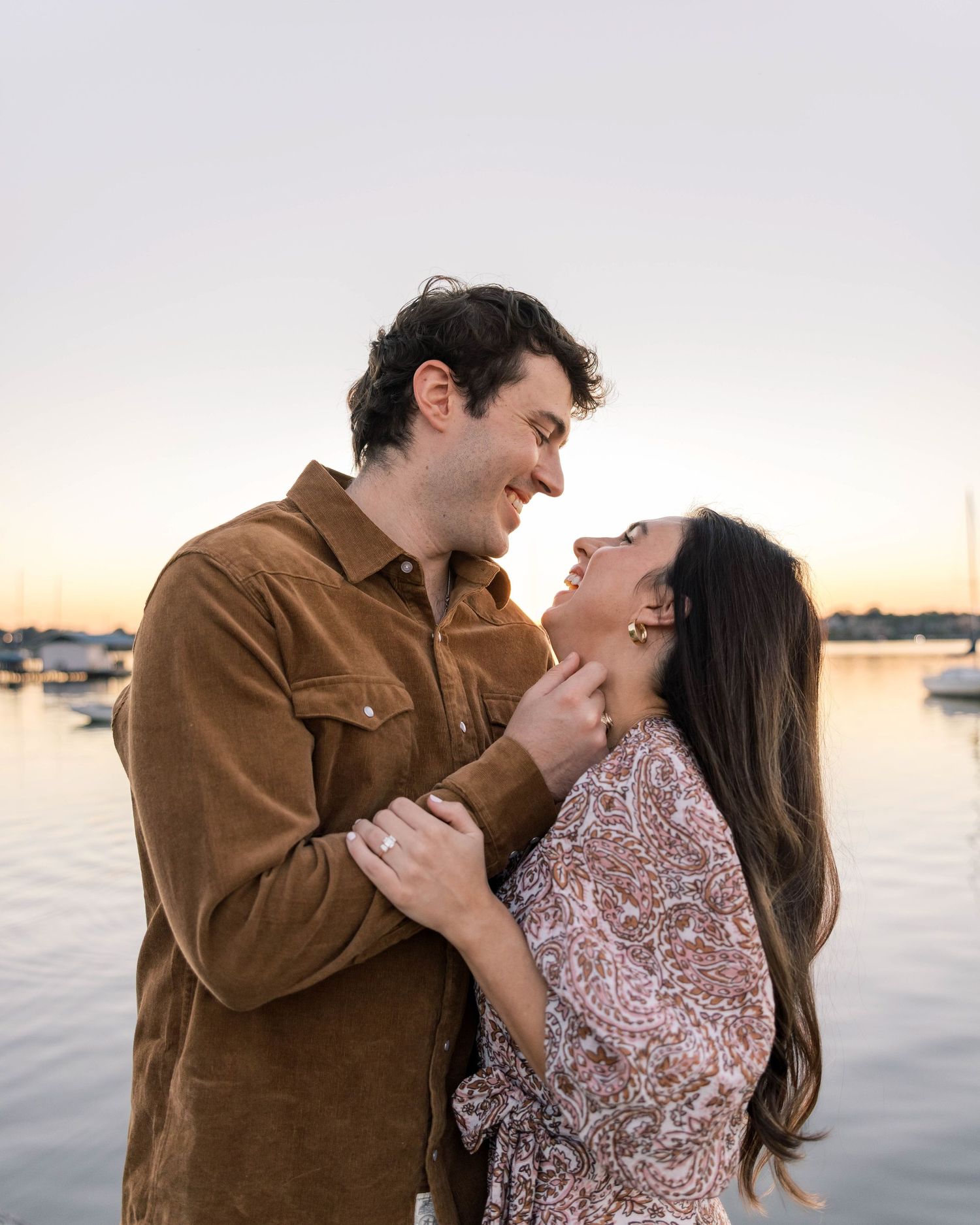 Couple sharing a romantic moment at sunset by the waterfront, smiling and gazing into each other's eyes.