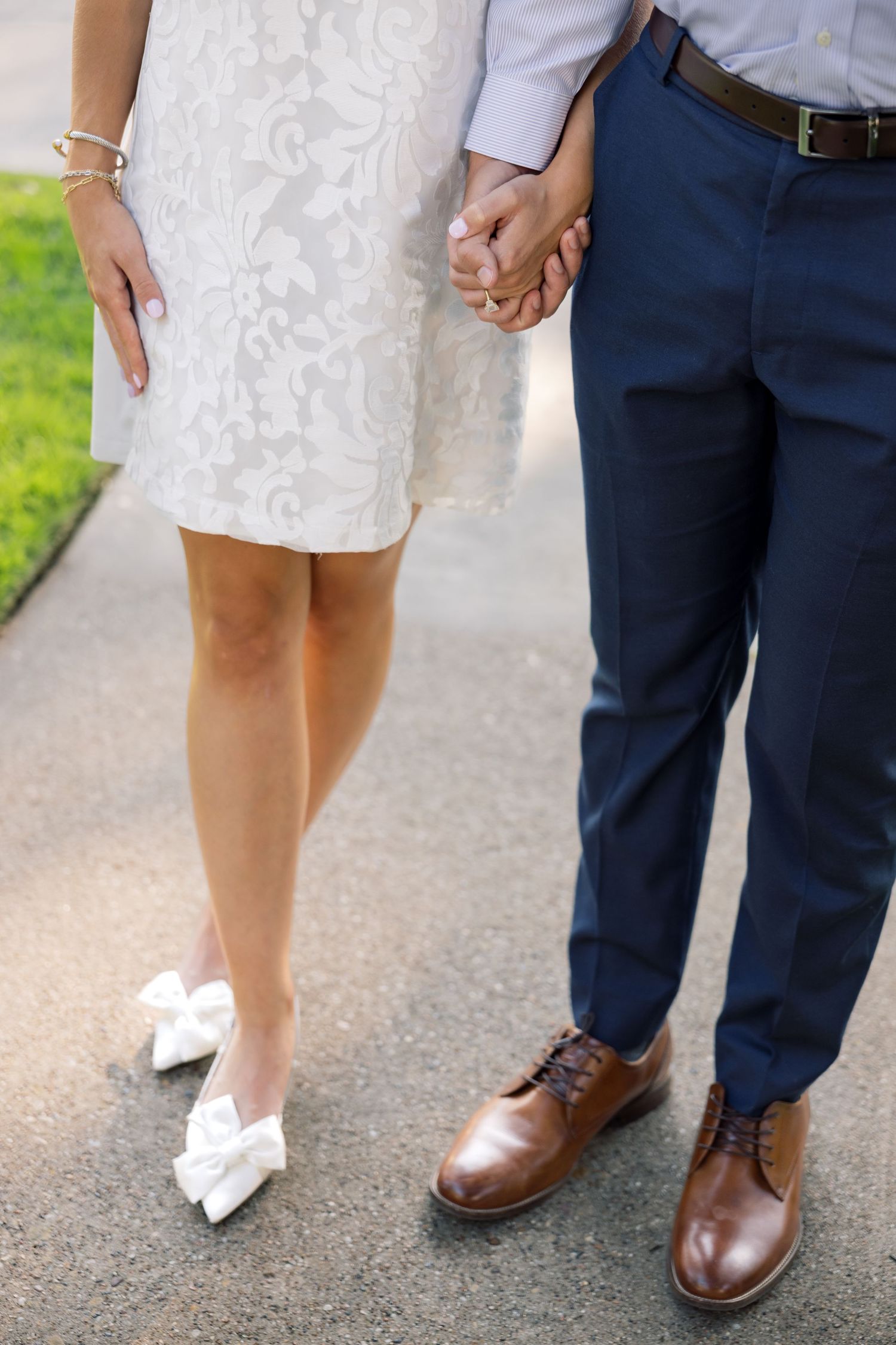 Couple holding hands, woman in white lace dress with bow flats, man in navy trousers and brown oxford shoes.