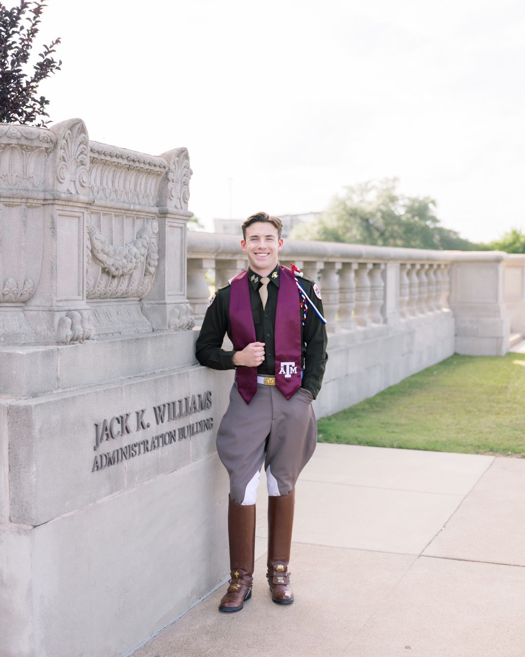Texas A&M graduate smiling in maroon stole and knickers outside Jack K. Williams Administration Building.