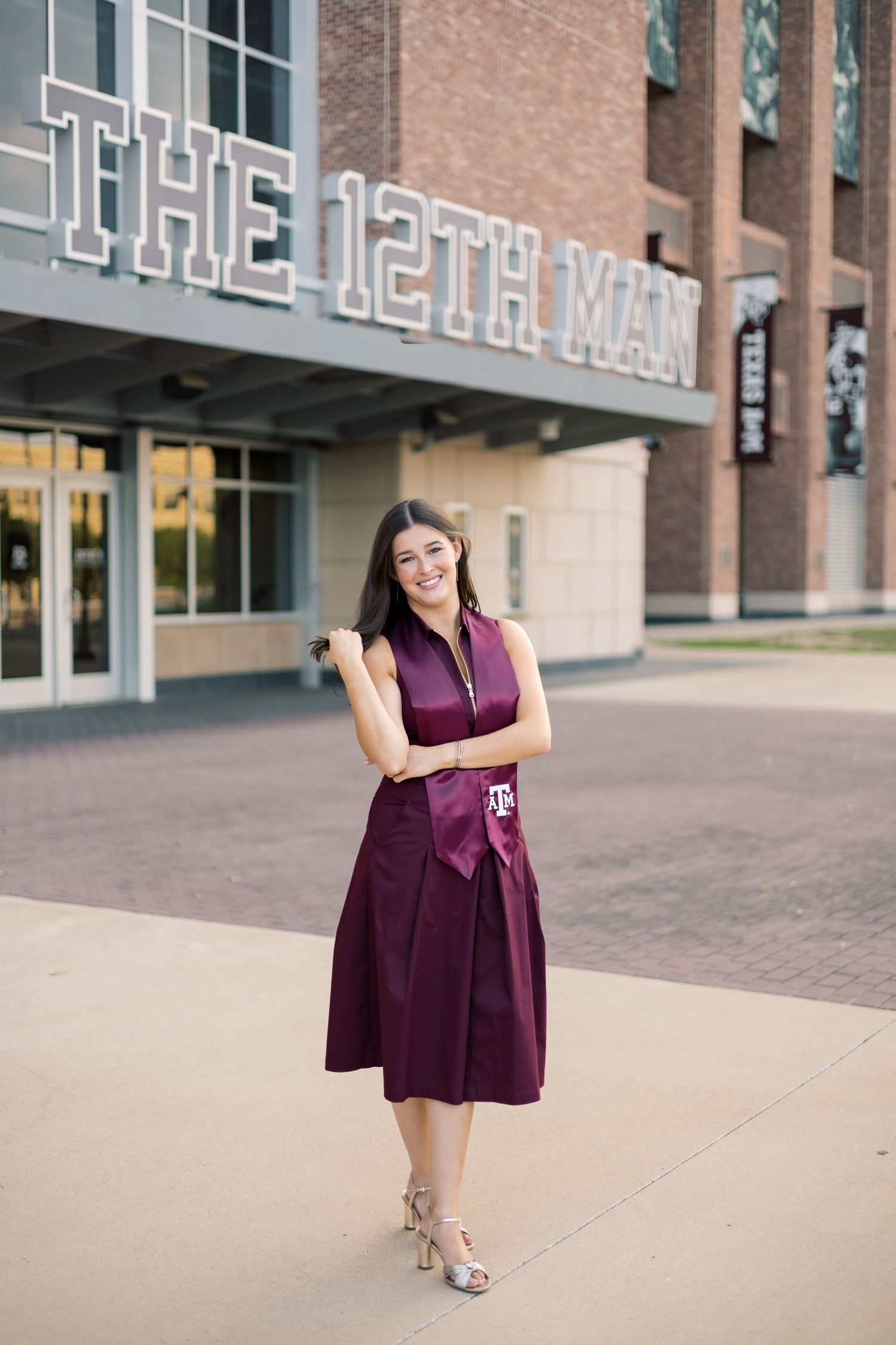 Smiling woman in maroon Texas A&M dress posing in front of The 12th Man stadium sign.