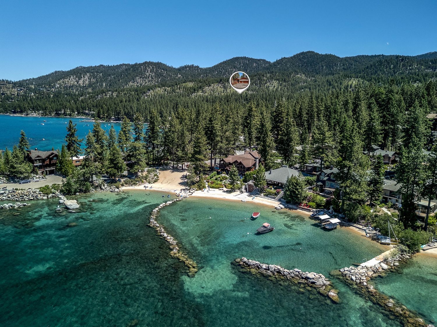 Aerial view of luxury Lake Tahoe waterfront estate with private beach, crystal-clear turquoise water, and dense pine forest backdrop.